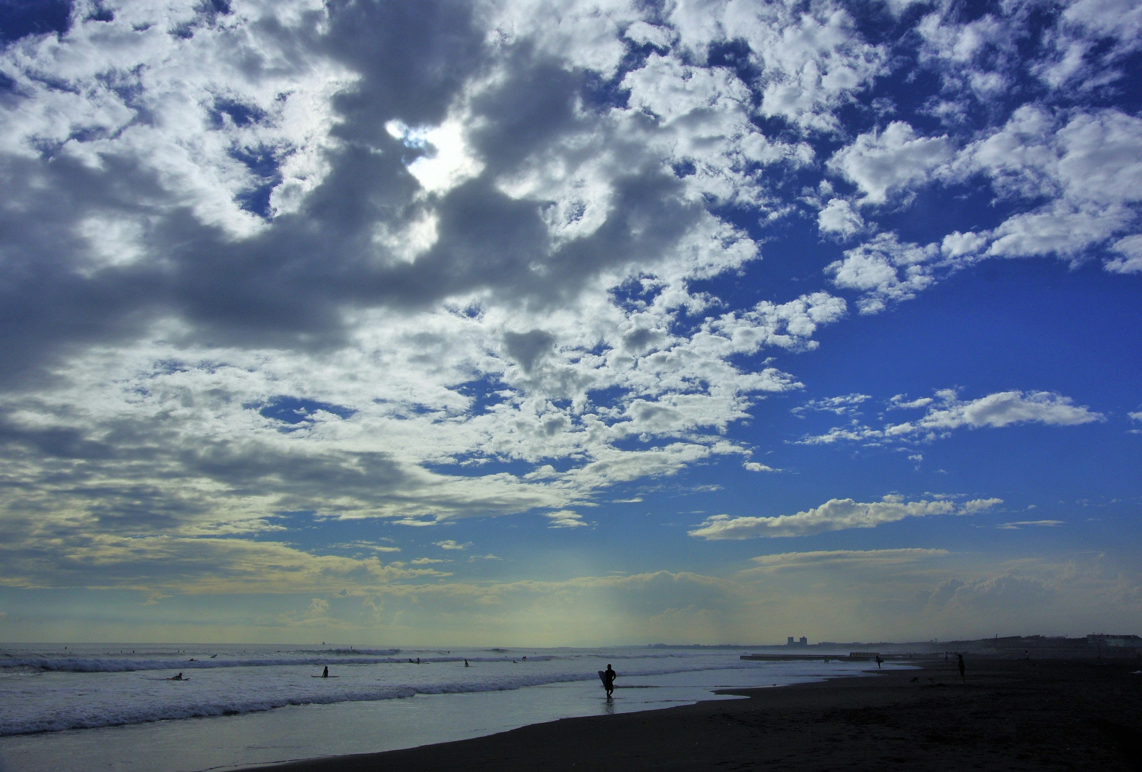 Escena de playa con cielo azul y nubes blancas con una persona caminando