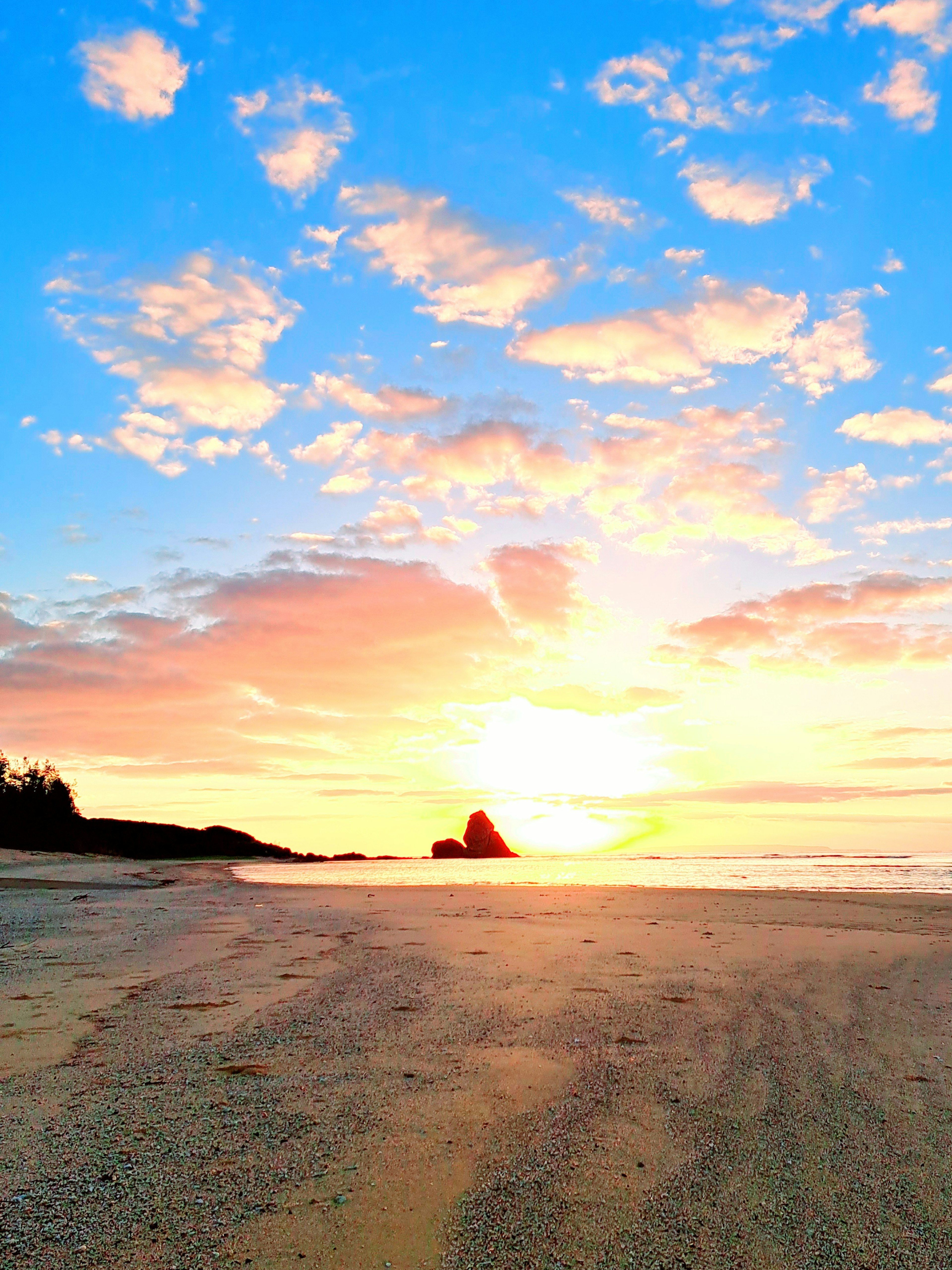 Pemandangan pantai saat matahari terbenam dengan warna cerah dan awan