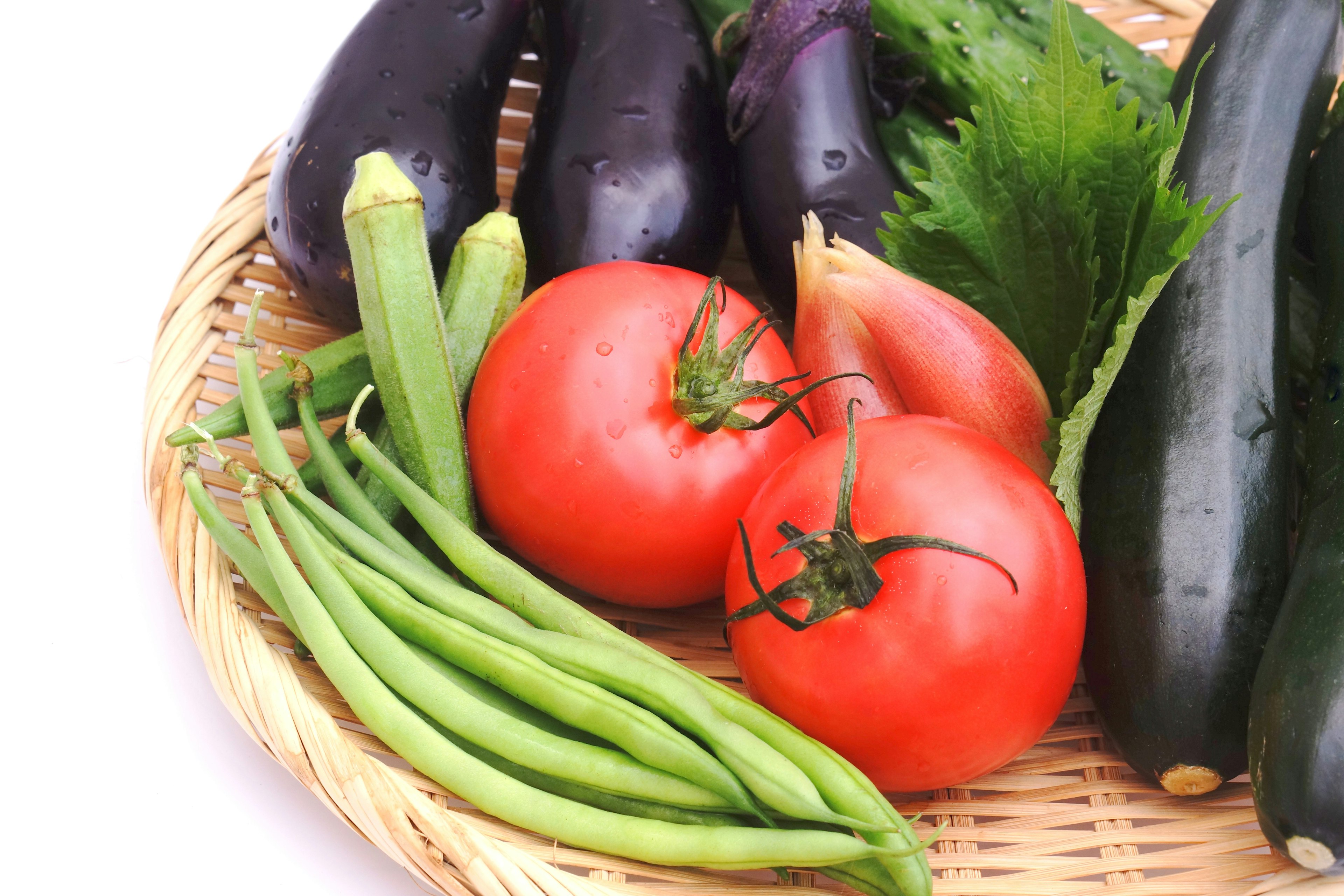 Verduras frescas en una cesta que incluye tomates, berenjenas, calabacines, judías verdes y lechuga