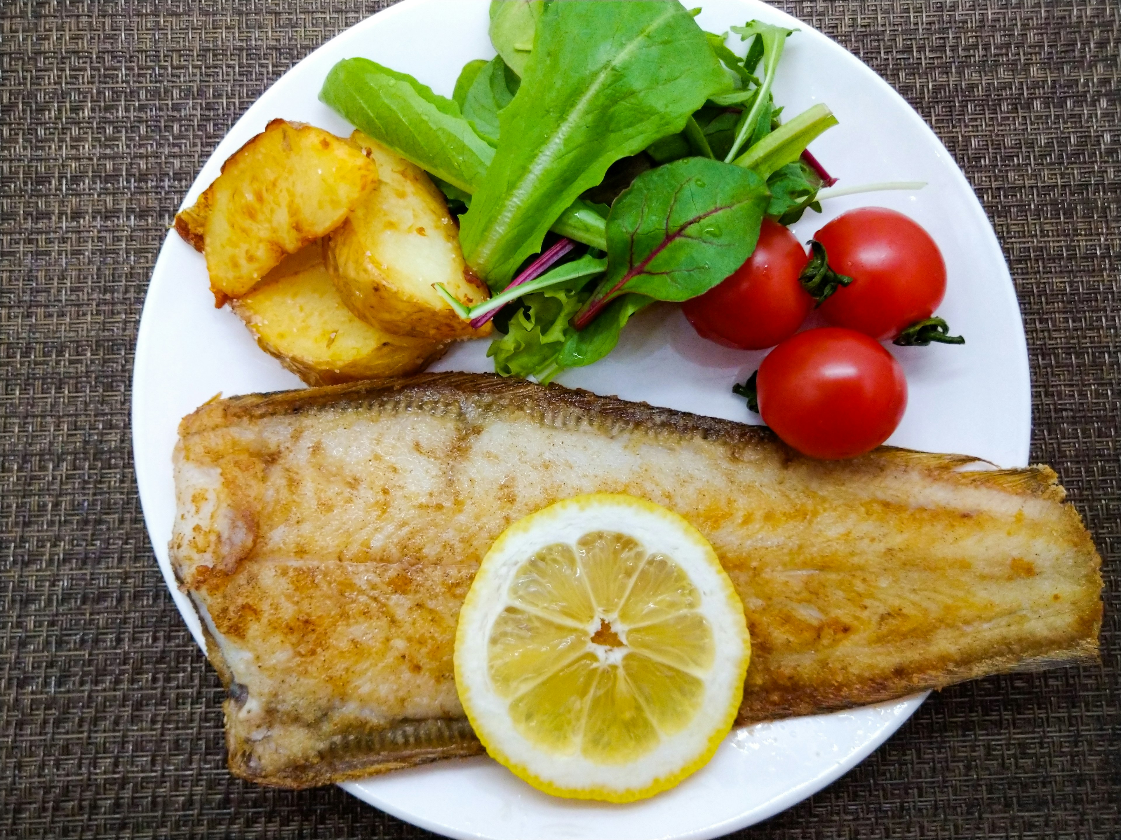 白身魚のグリルとレモンのスライスの上に新鮮なサラダとトマトが添えられたプレート