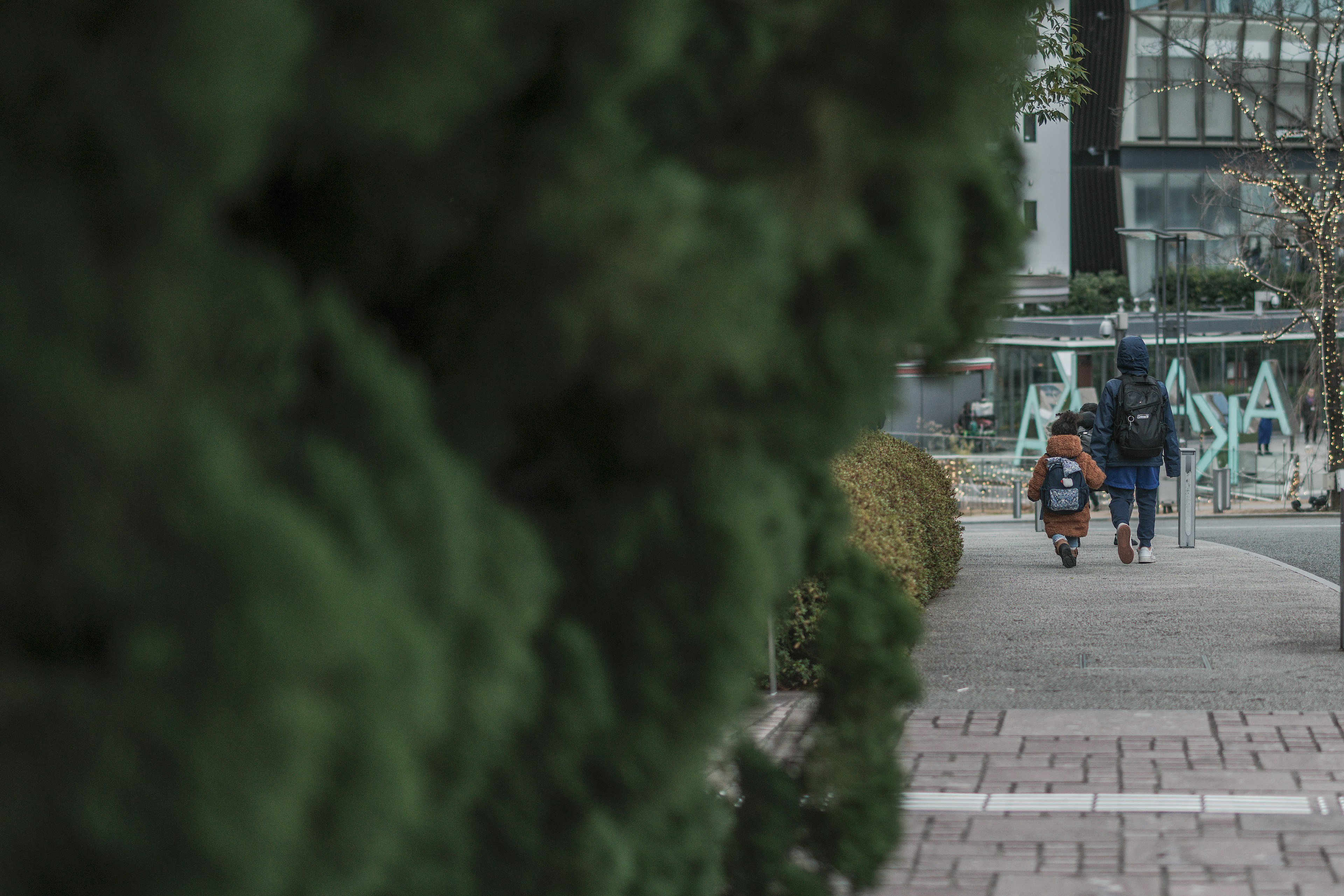 緑の植物の前を歩く二人の人物が見える街の風景