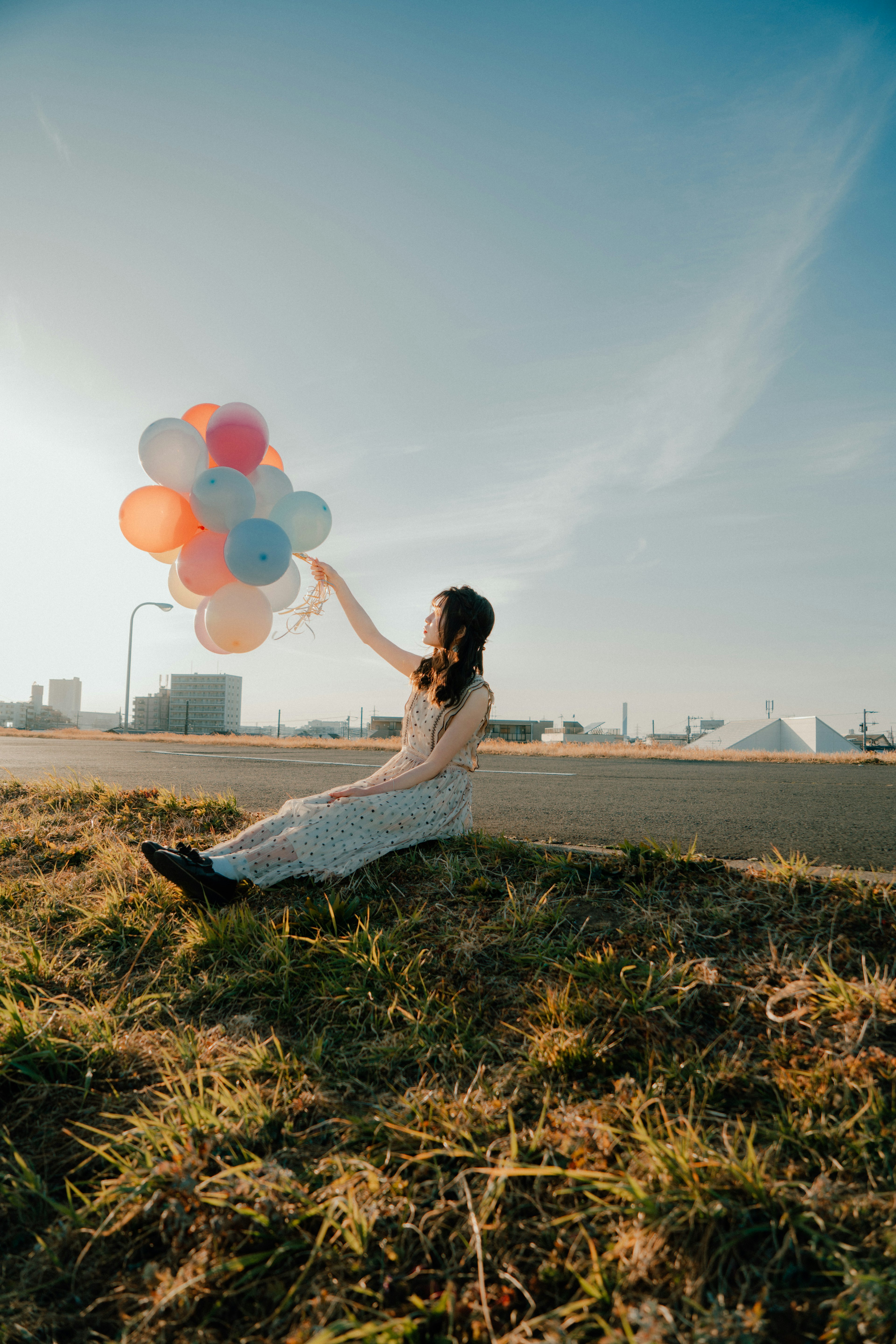 青空の下でカラフルな風船を持つ女性が座っている風景