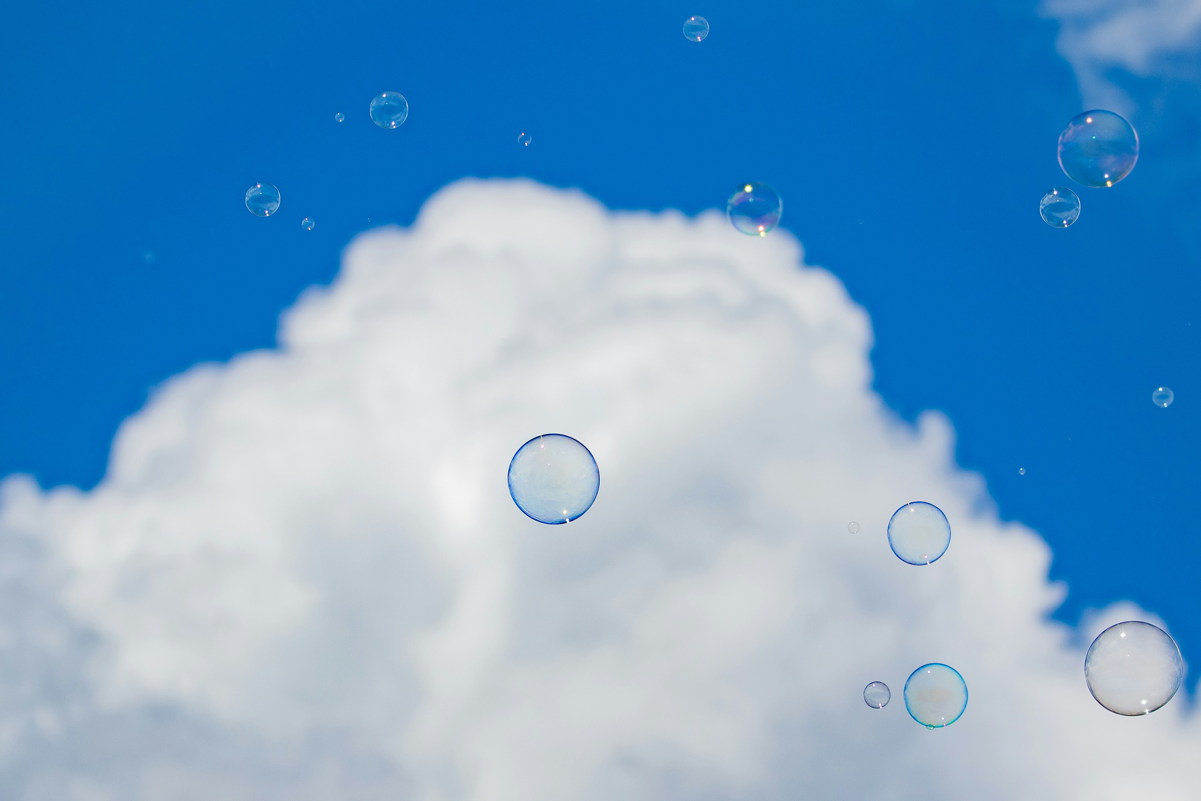 Seifenblasen, die in einem blauen Himmel mit weißen Wolken schweben