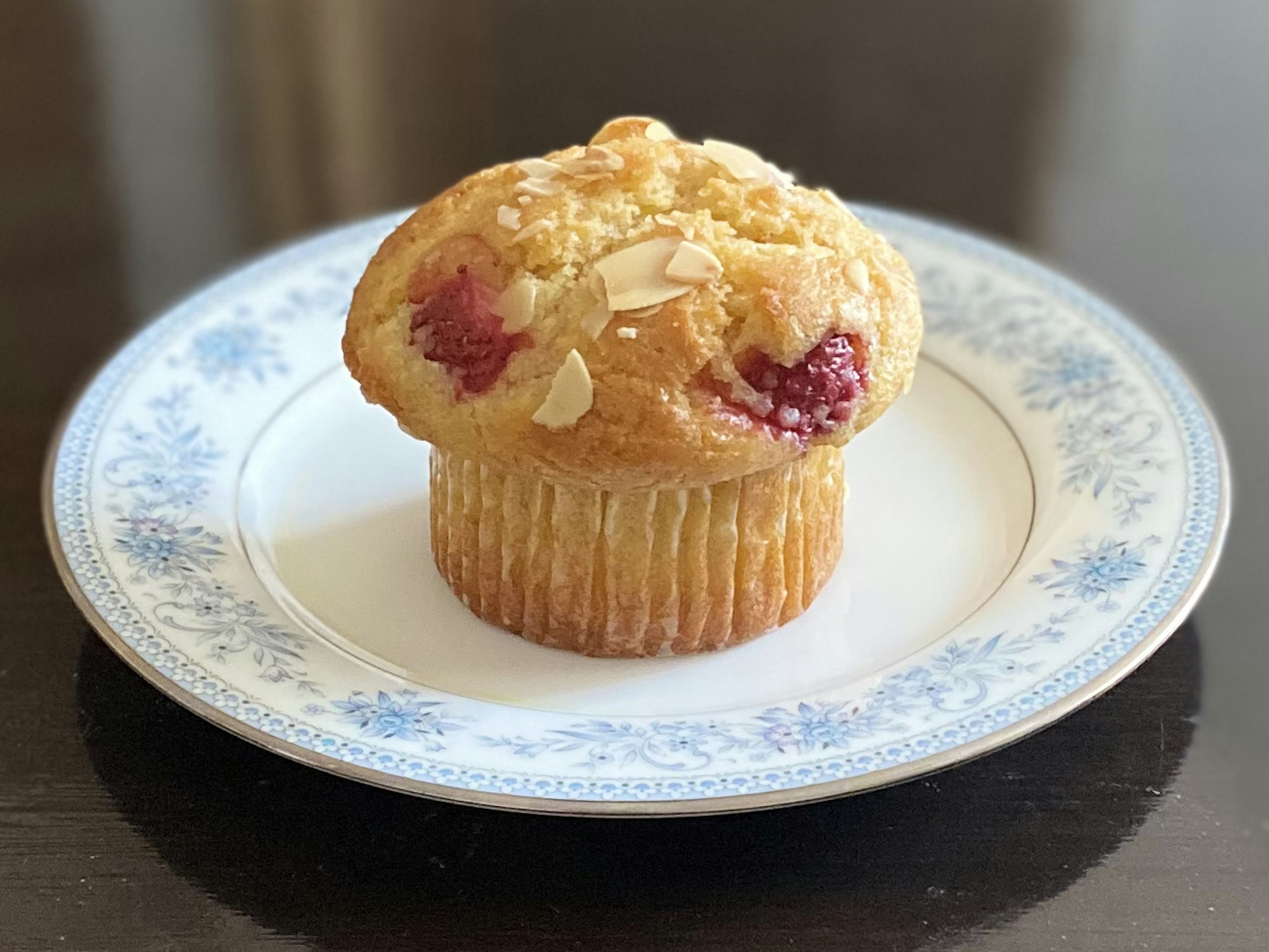 Ein Himbeermuffin mit Mandeln auf einem blauen Blumenteller