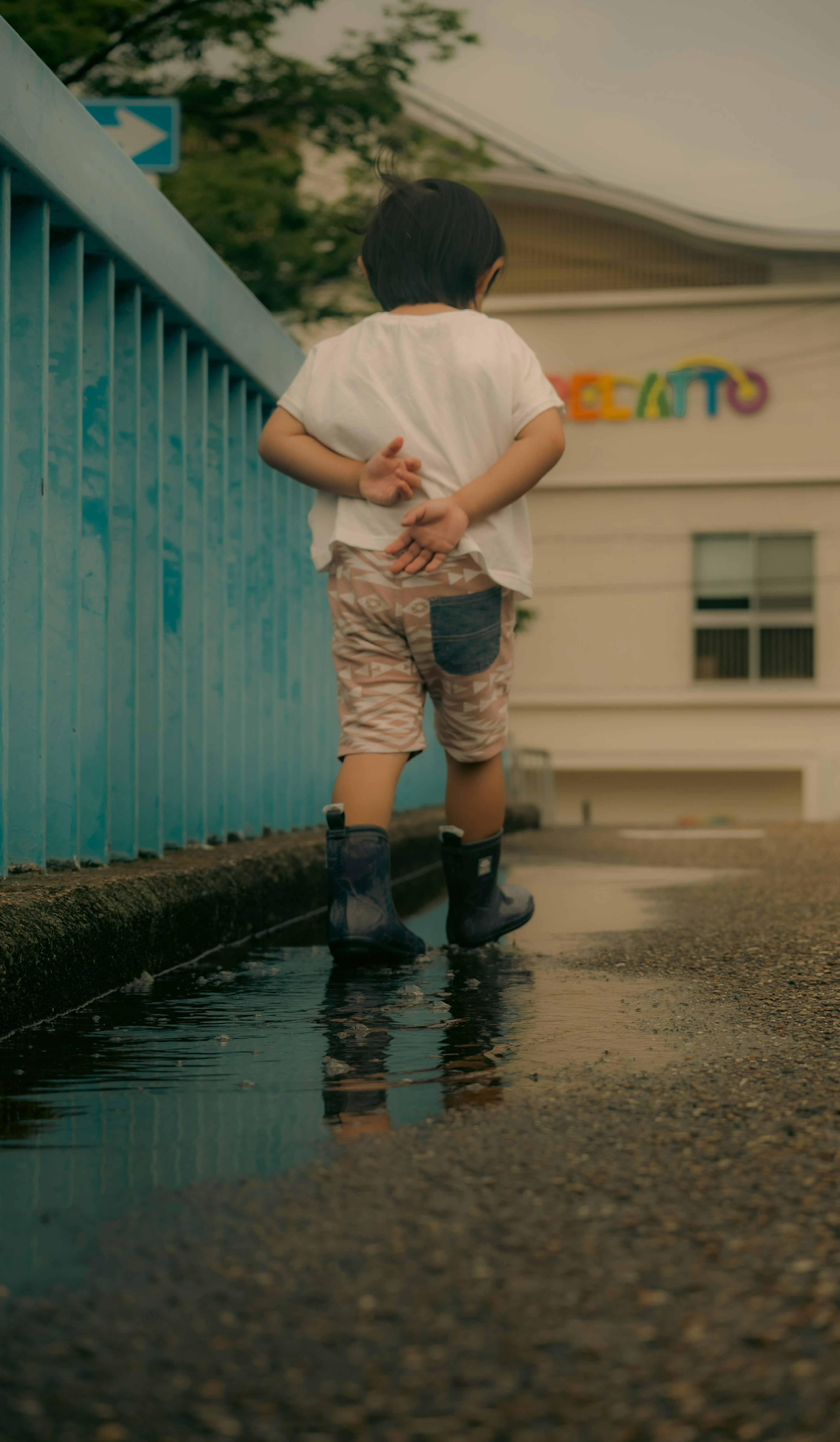 青い橋のそばで水たまりを歩く子供の後ろ姿