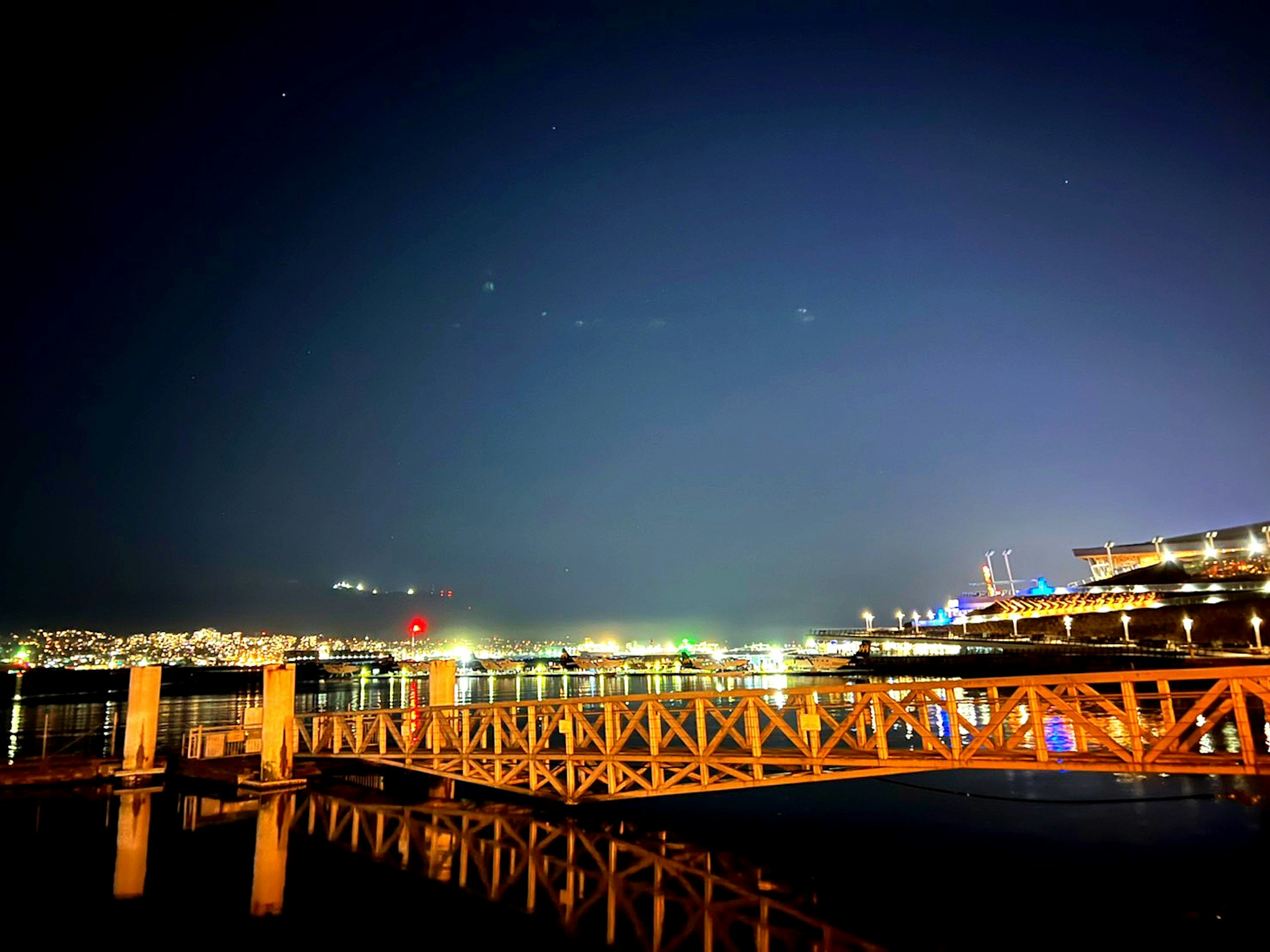 Dermaga kayu di malam hari dengan pantulan dan lampu kota