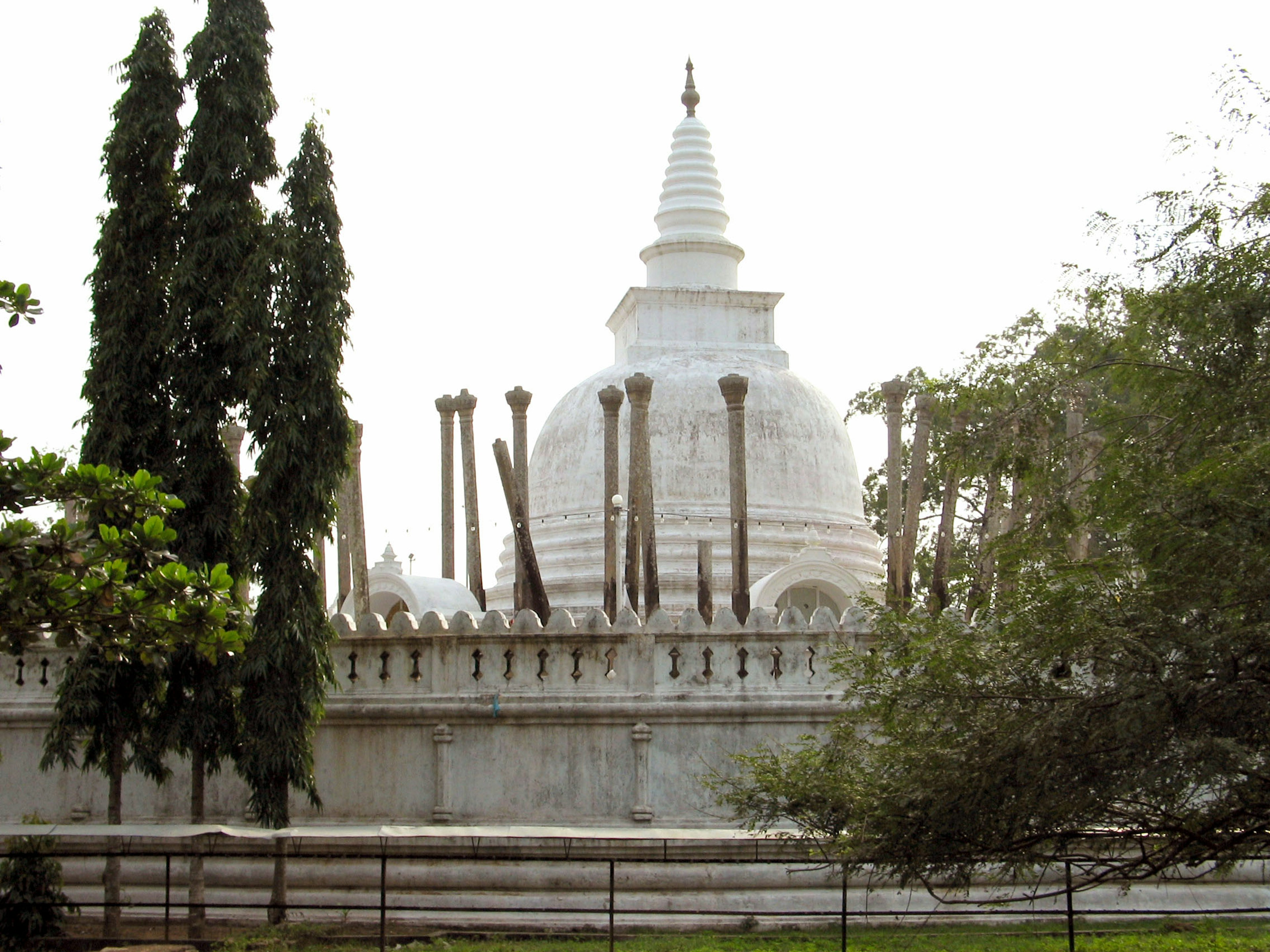 Blick auf eine weiße Stupa, umgeben von hohen Bäumen