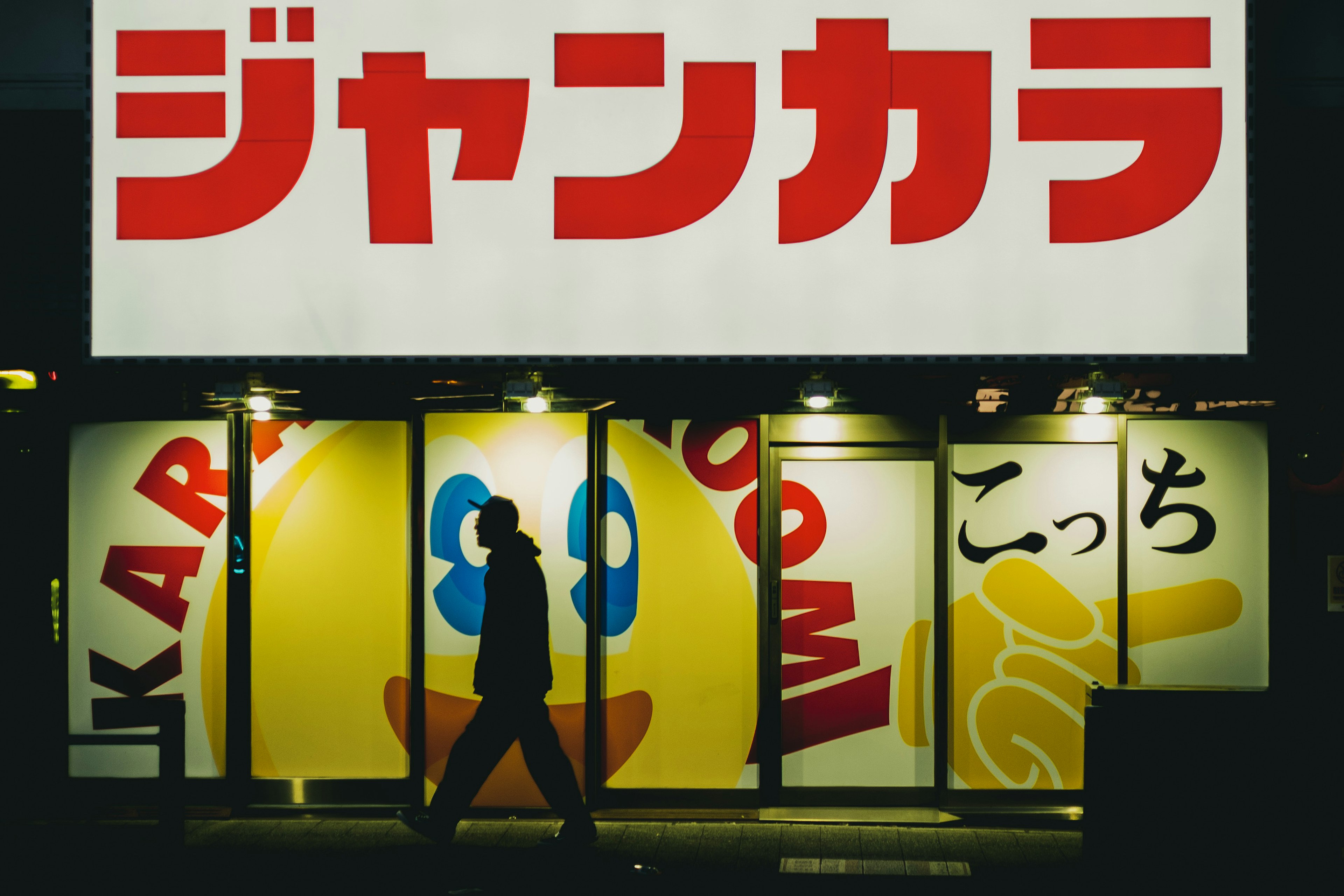 A person walking in the night with bright signage in the background