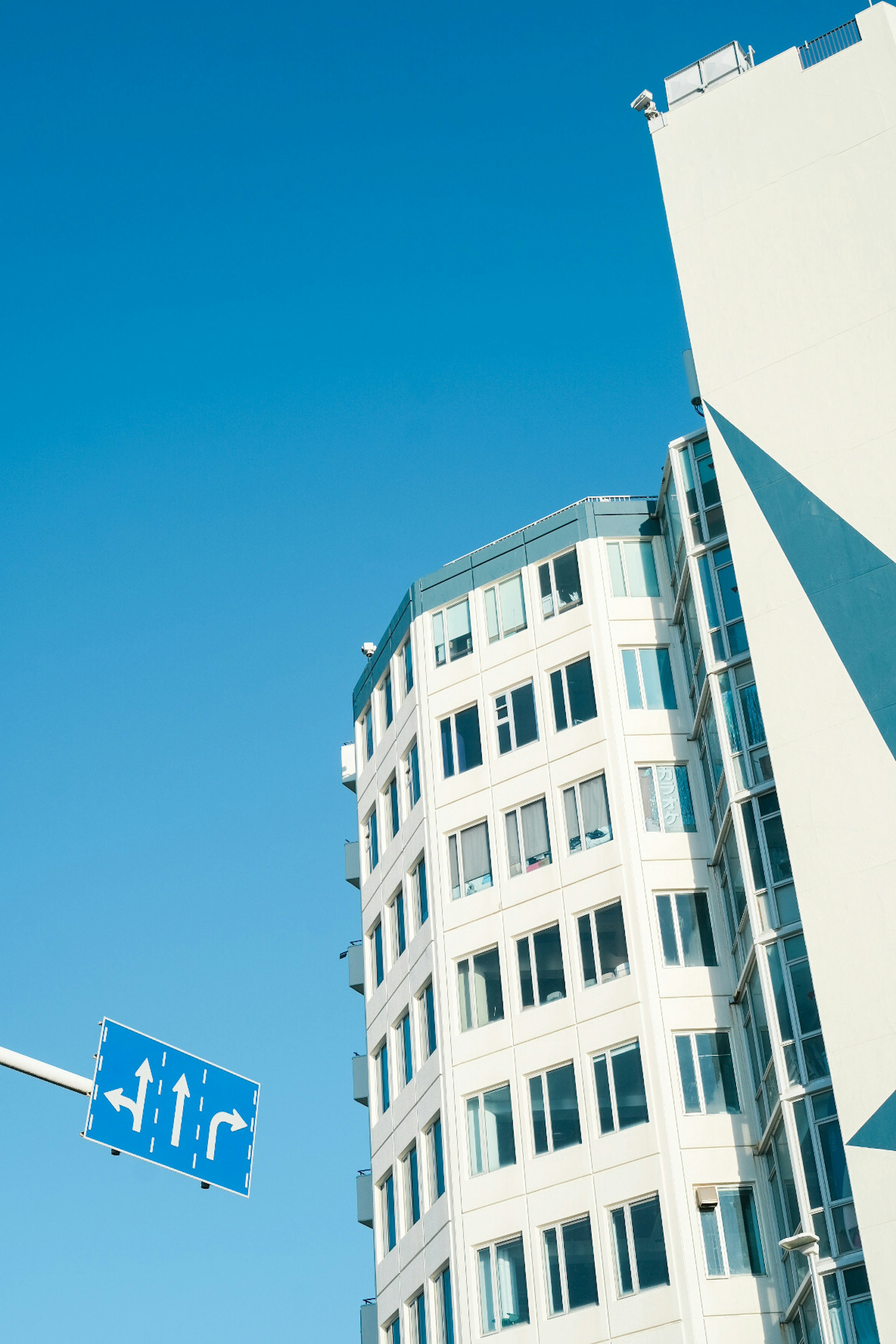 Edificio curvo bajo un cielo azul con señal direccional