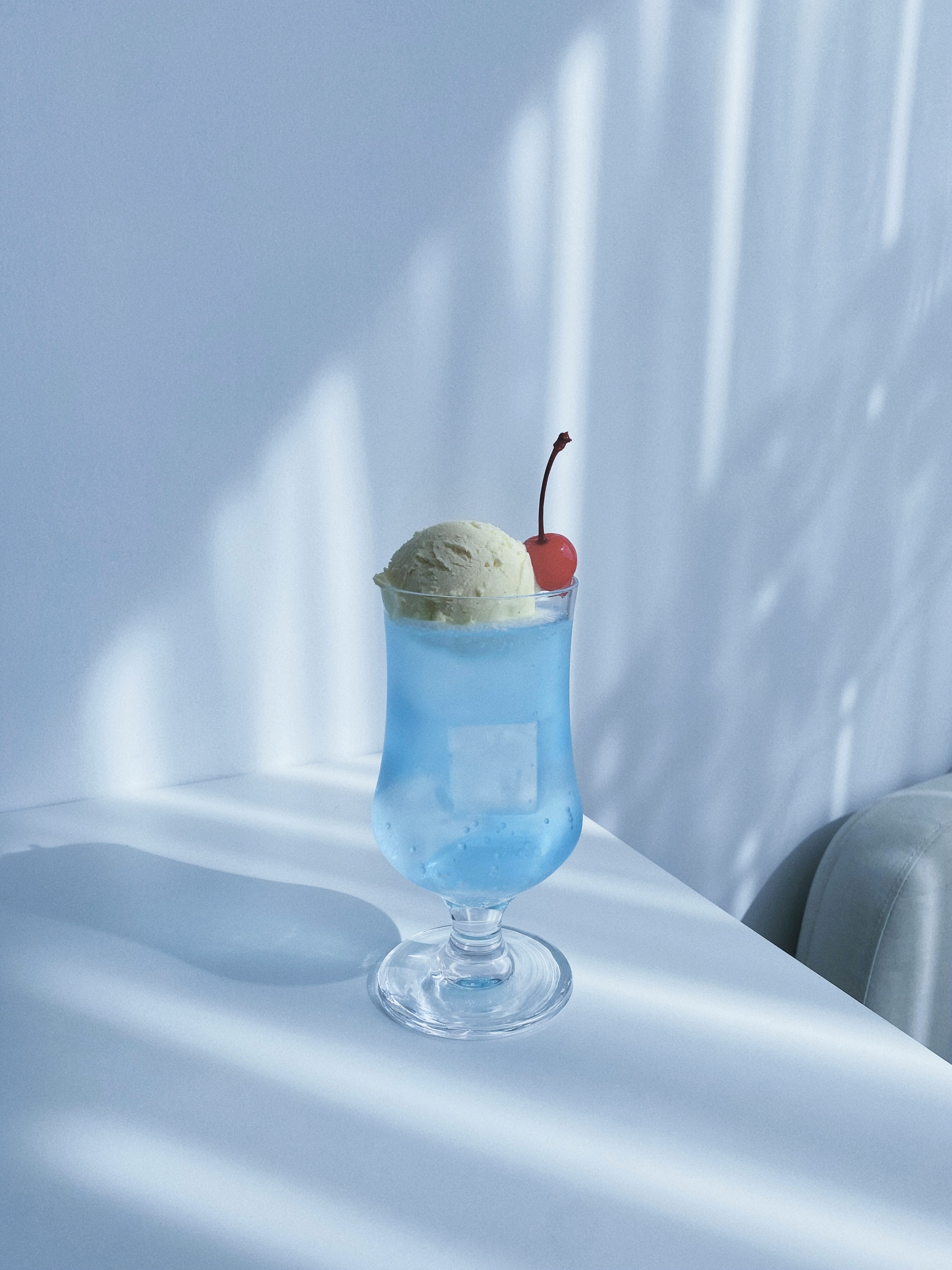 A blue drink topped with ice cream and a cherry in a glass