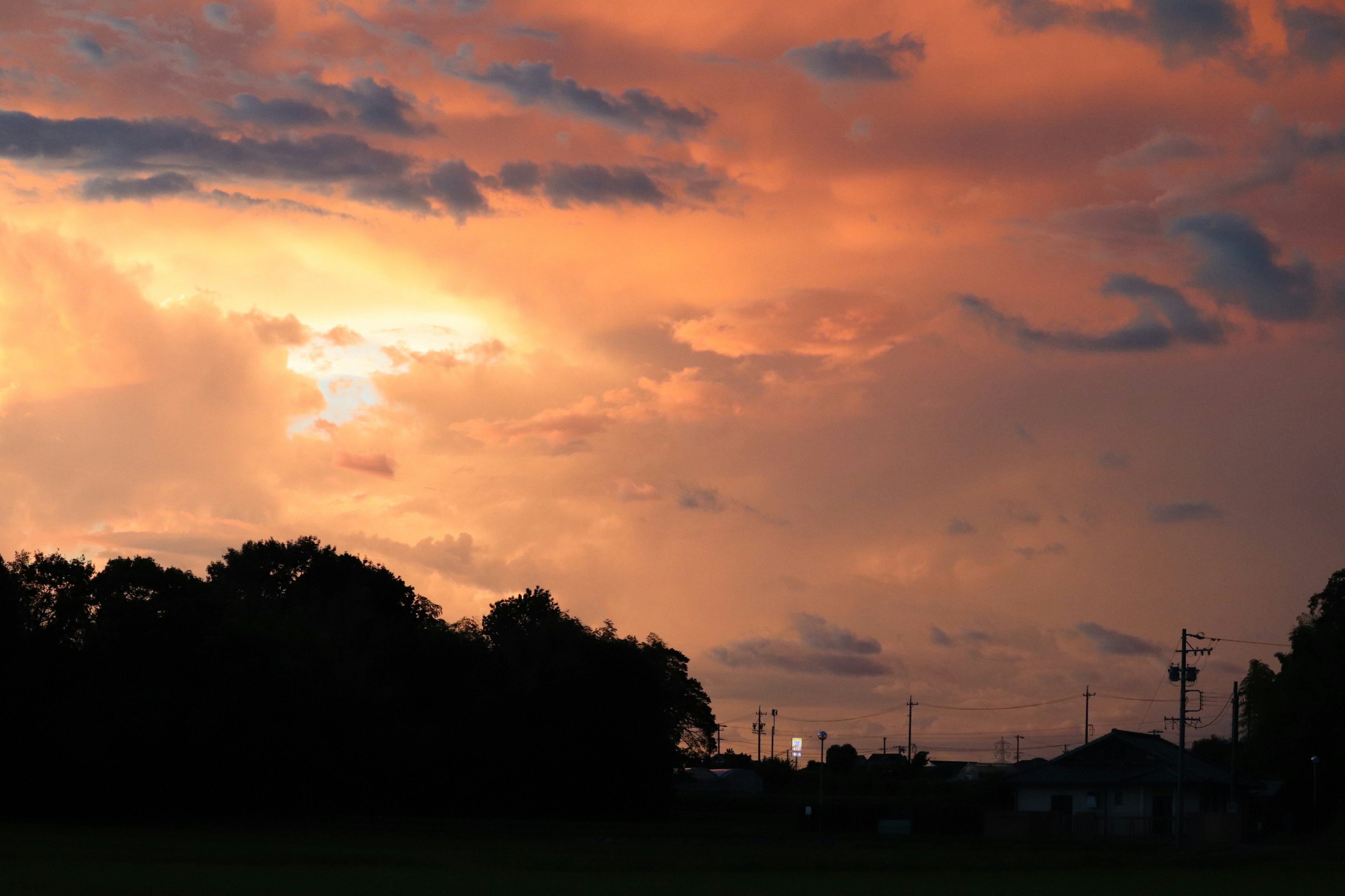 Un paesaggio con un cielo al tramonto con sfumature di arancione e viola nuvole sagomate da alberi