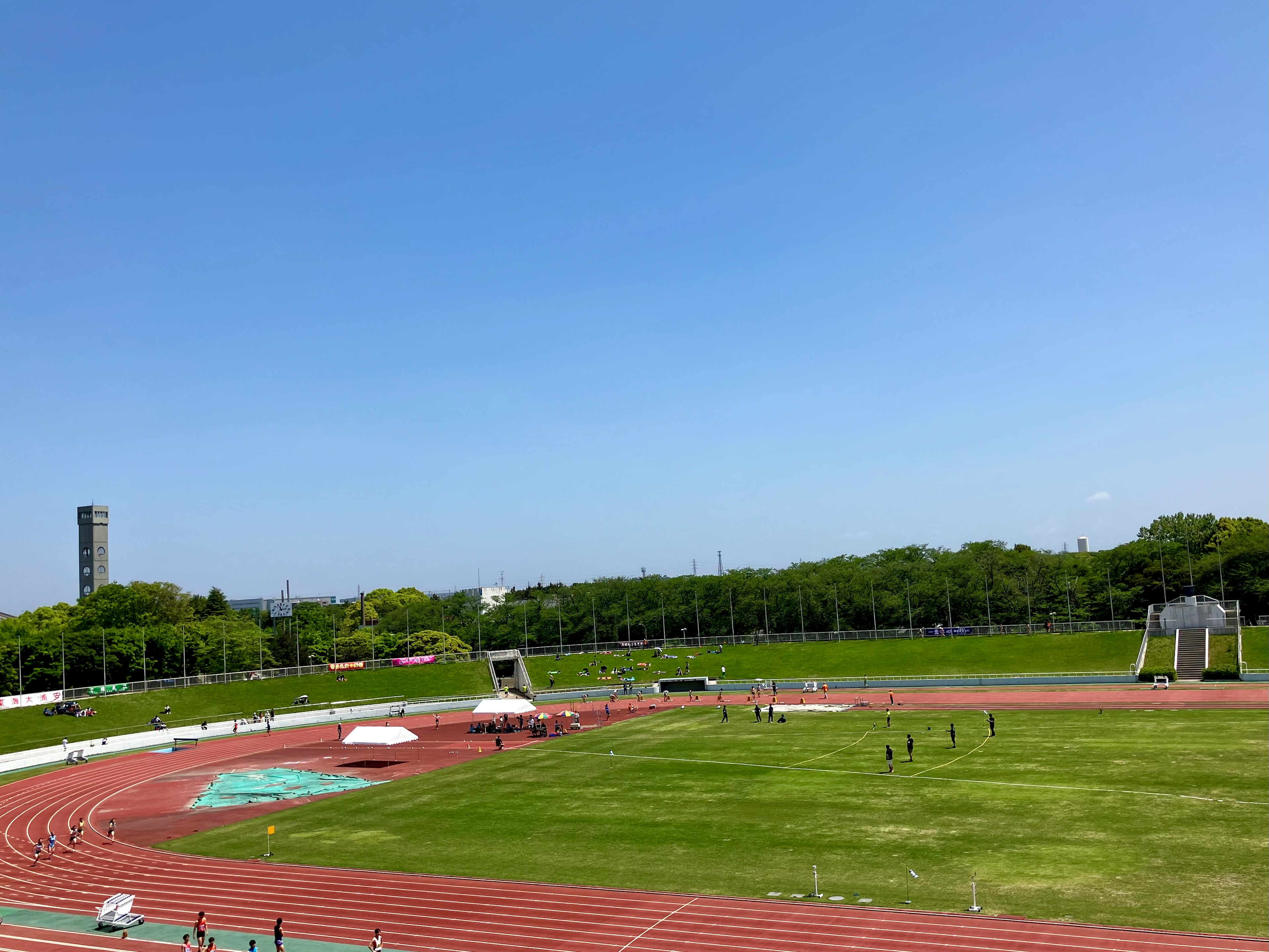 青空の下に広がる陸上競技場の風景 緑の芝生と赤いトラックが特徴