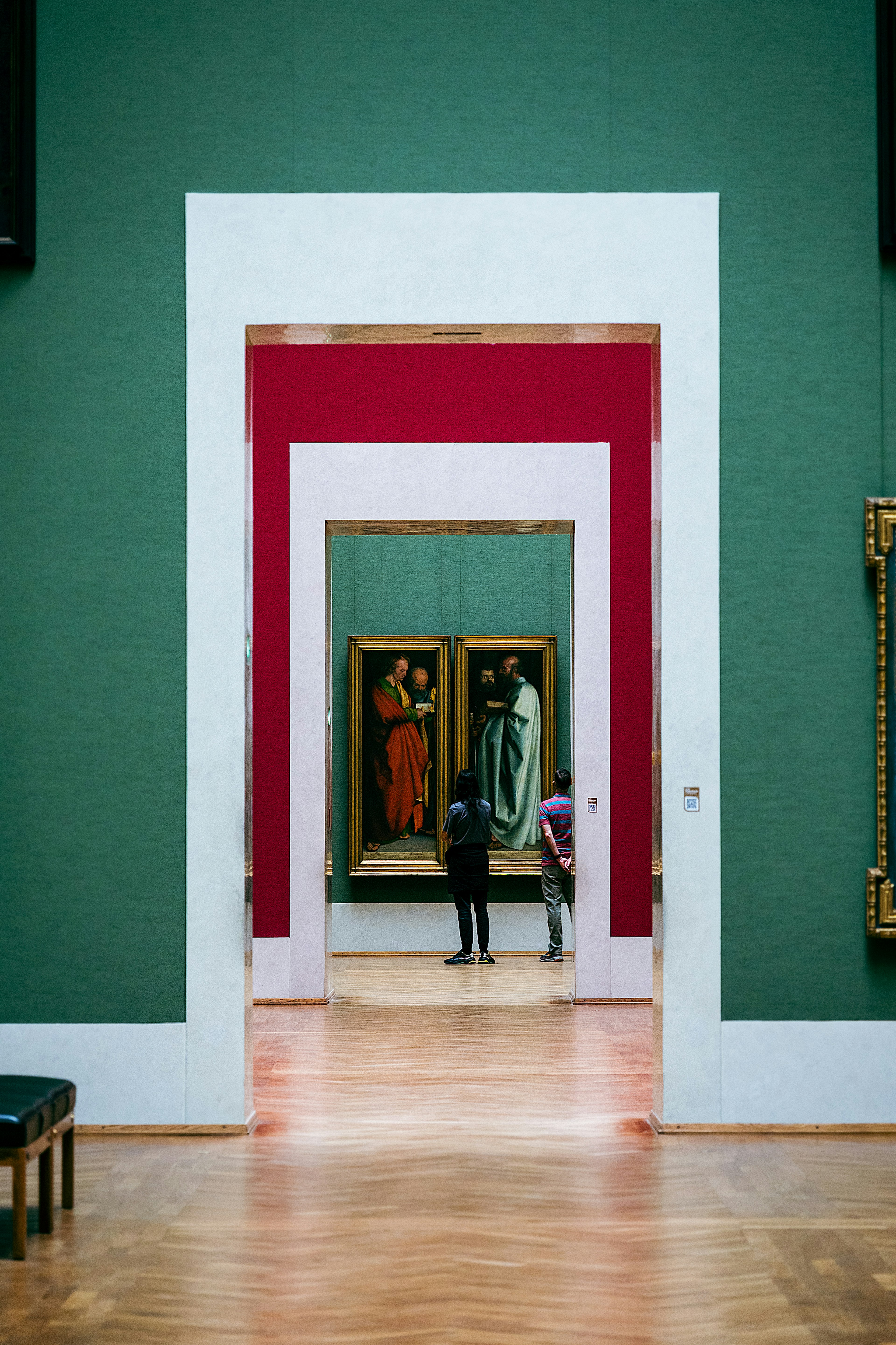 Un couloir dans un musée avec des murs verts présentant des arches encadrées de rouge et des peintures