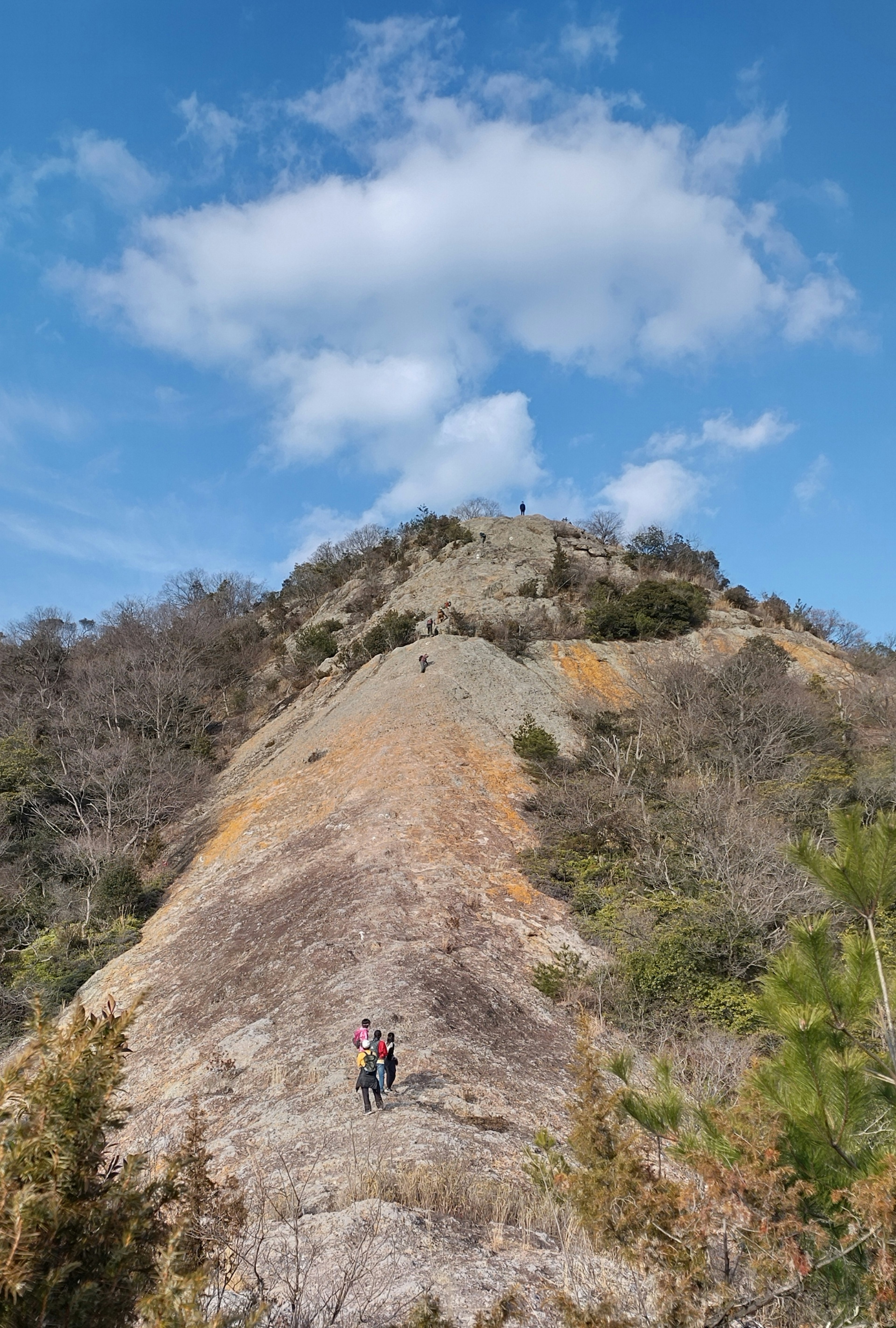 在藍天和蓬鬆雲朵下的岩石山坡上的登山者