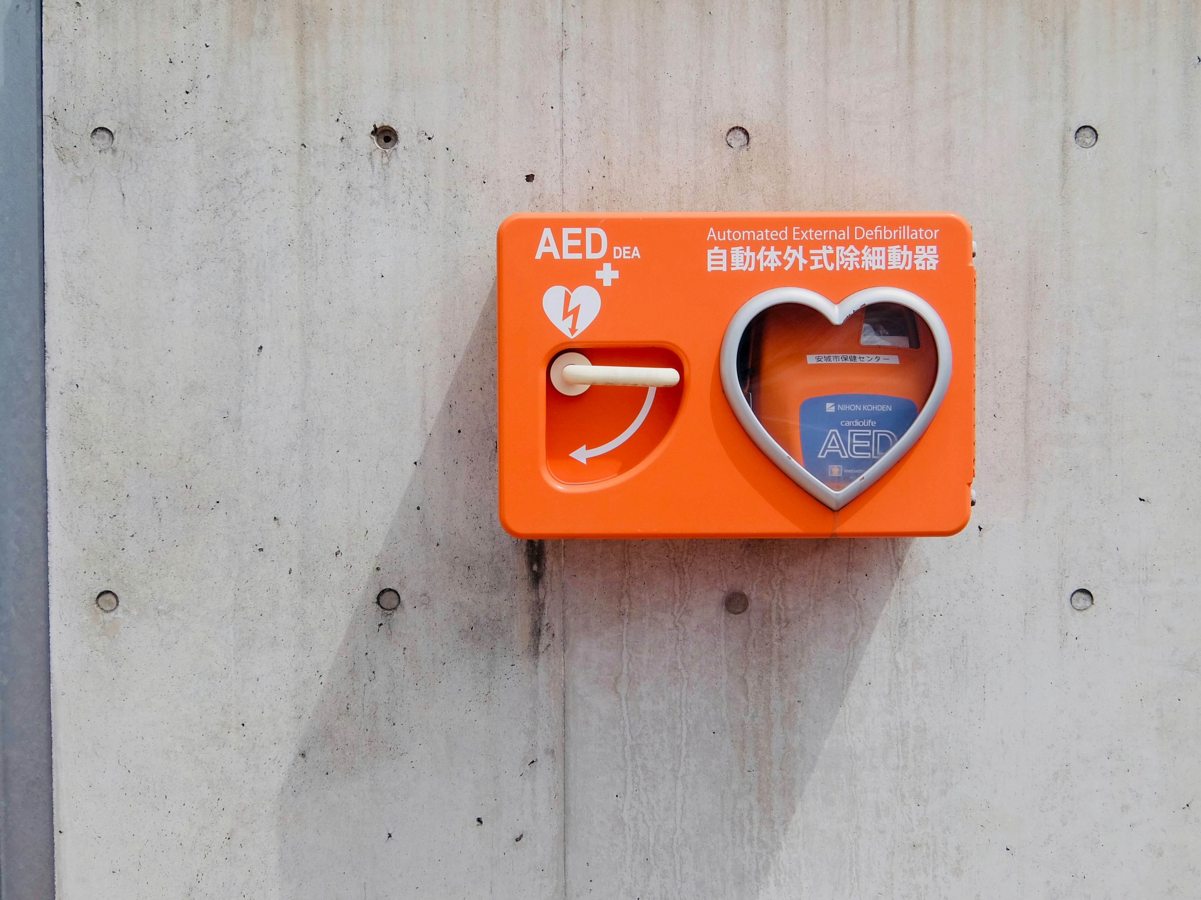 Boîte AED orange fixée sur un mur en béton