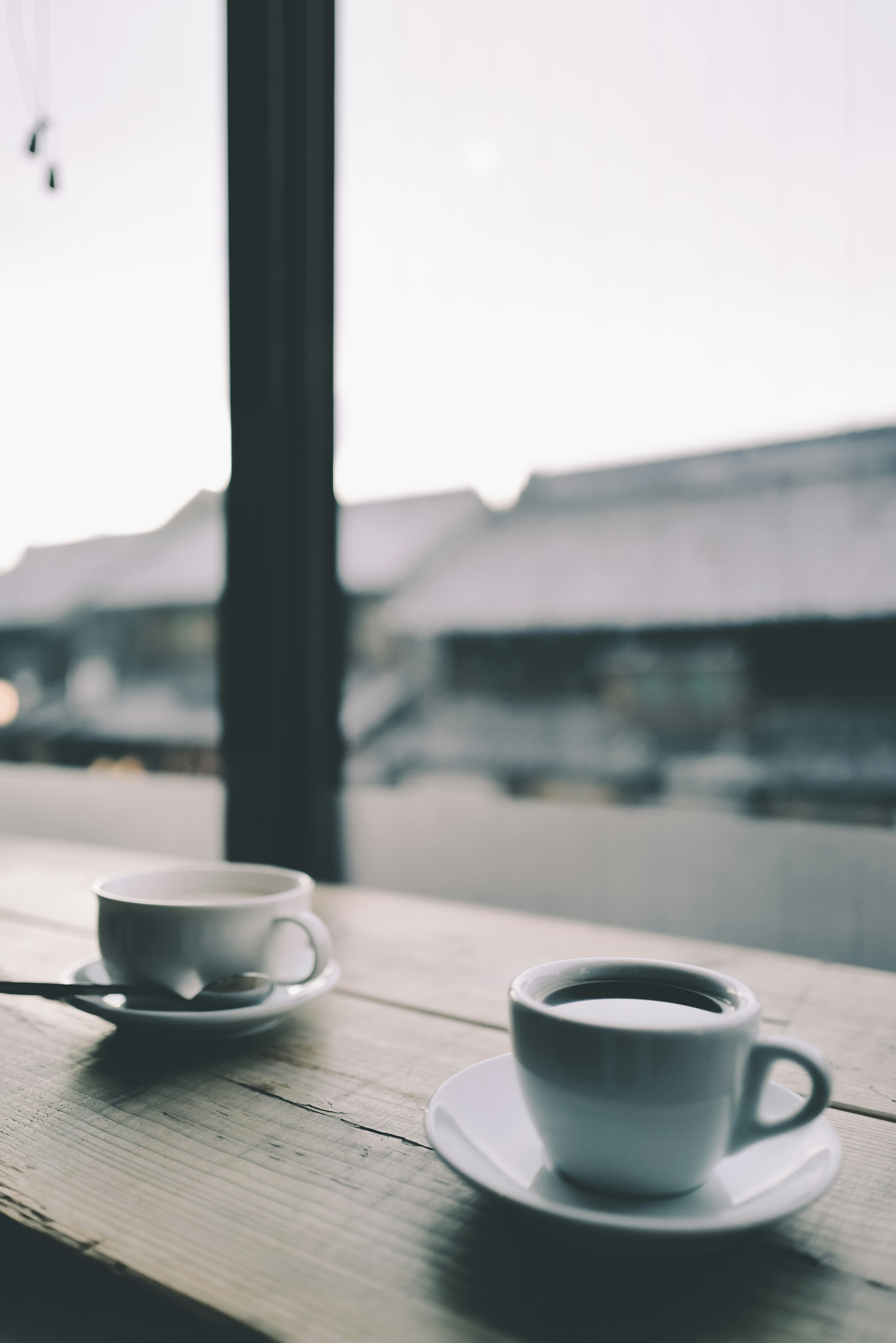 Two coffee cups on a wooden table by a window