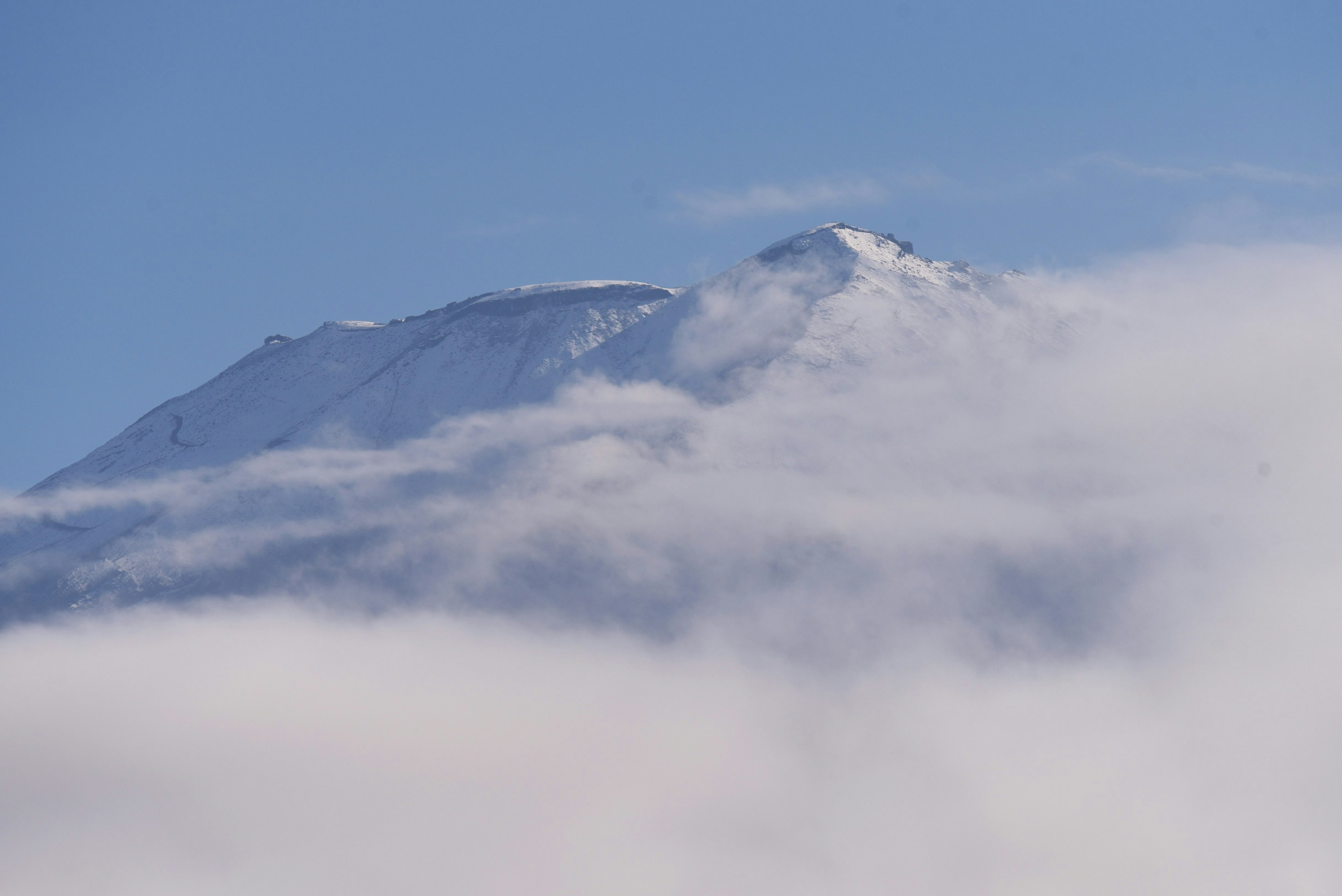 Puncak gunung bersalju muncul dari awan di bawah langit biru