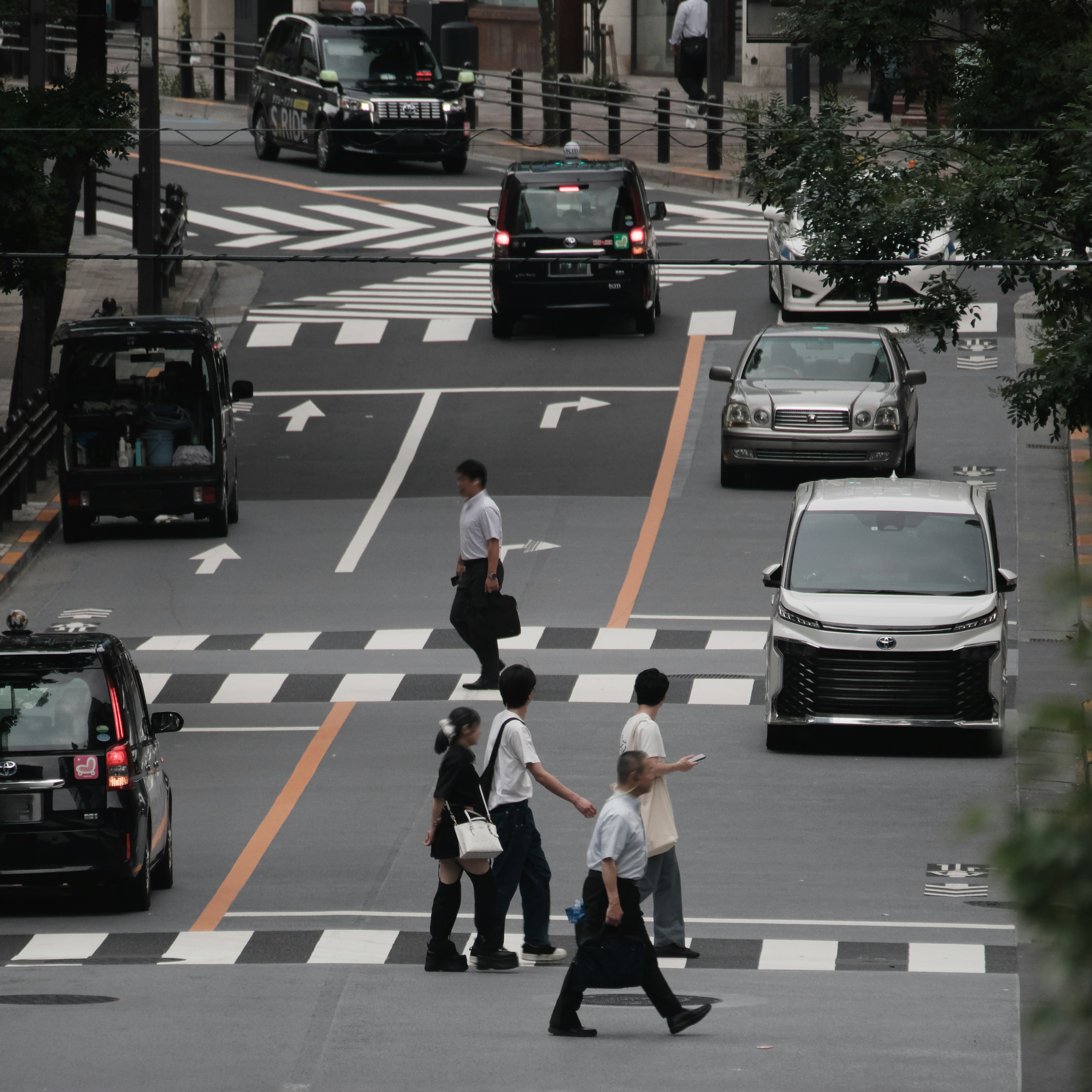 ผู้คนข้ามถนนที่สี่แยกในเมืองโดยมีรถยนต์