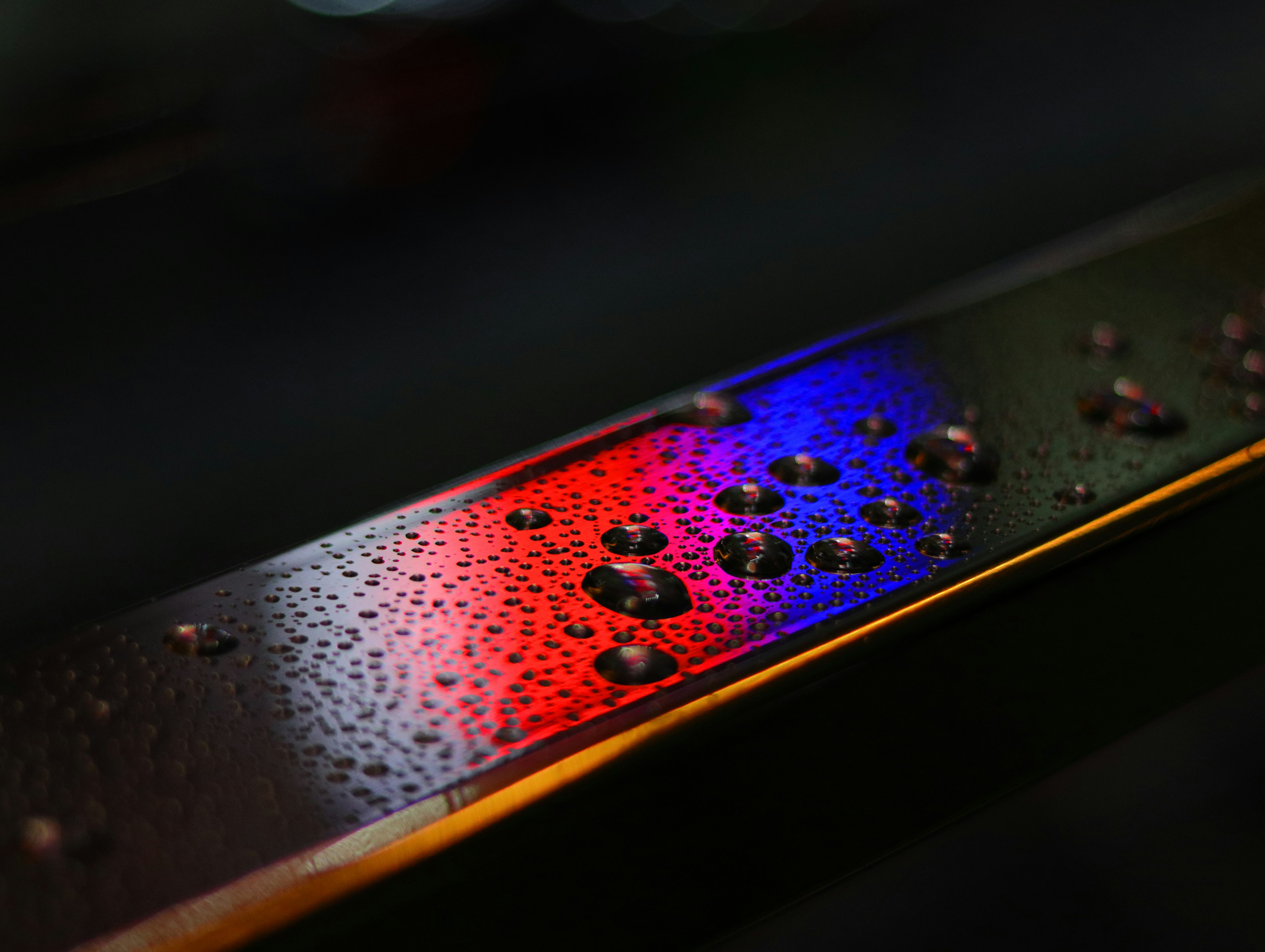 Glossy surface with water droplets reflecting red and blue light