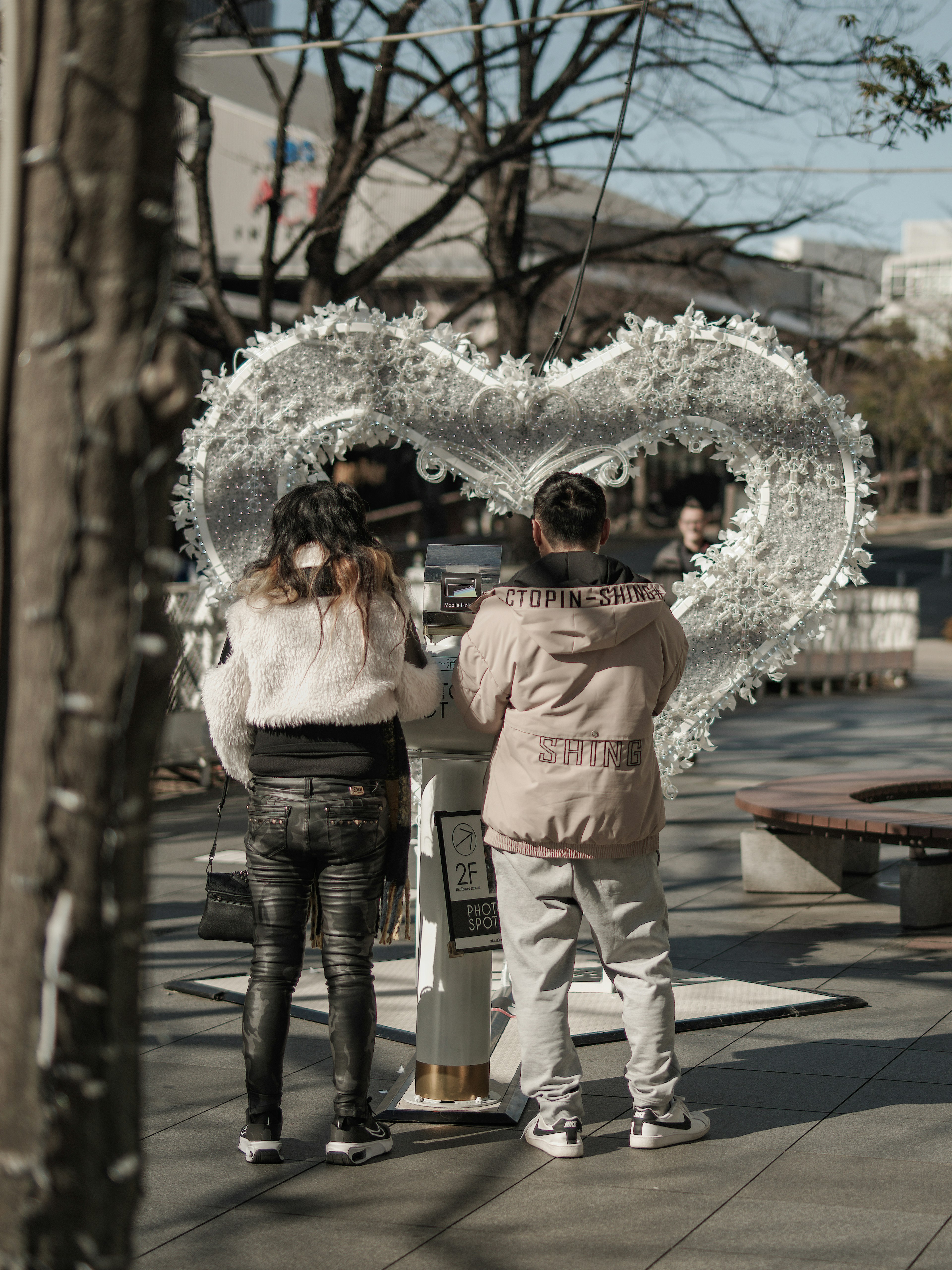 Two people standing in front of a large white heart-shaped display in a park