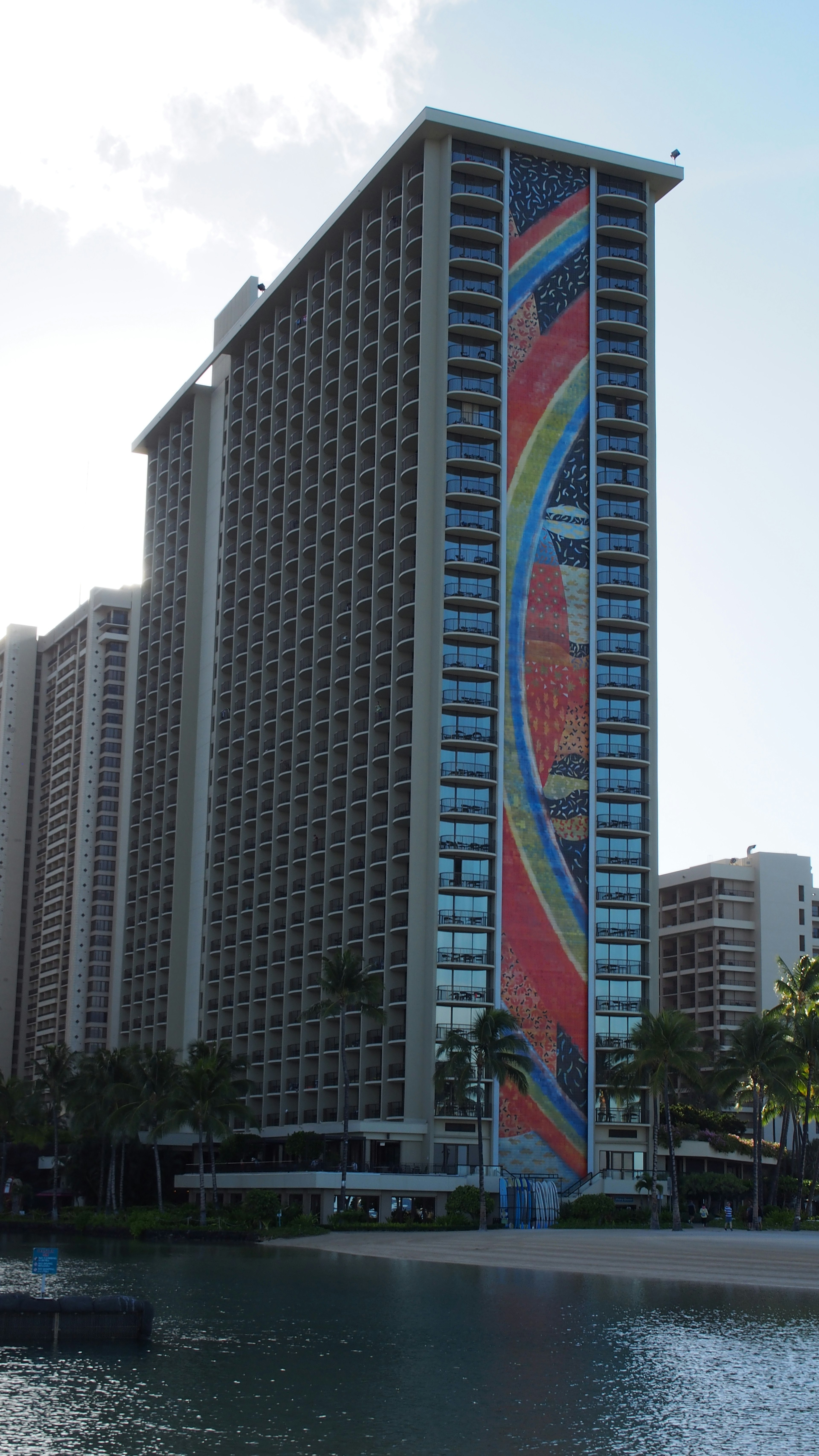 Colorful mural on a high-rise building in Hawaii with surrounding palm trees