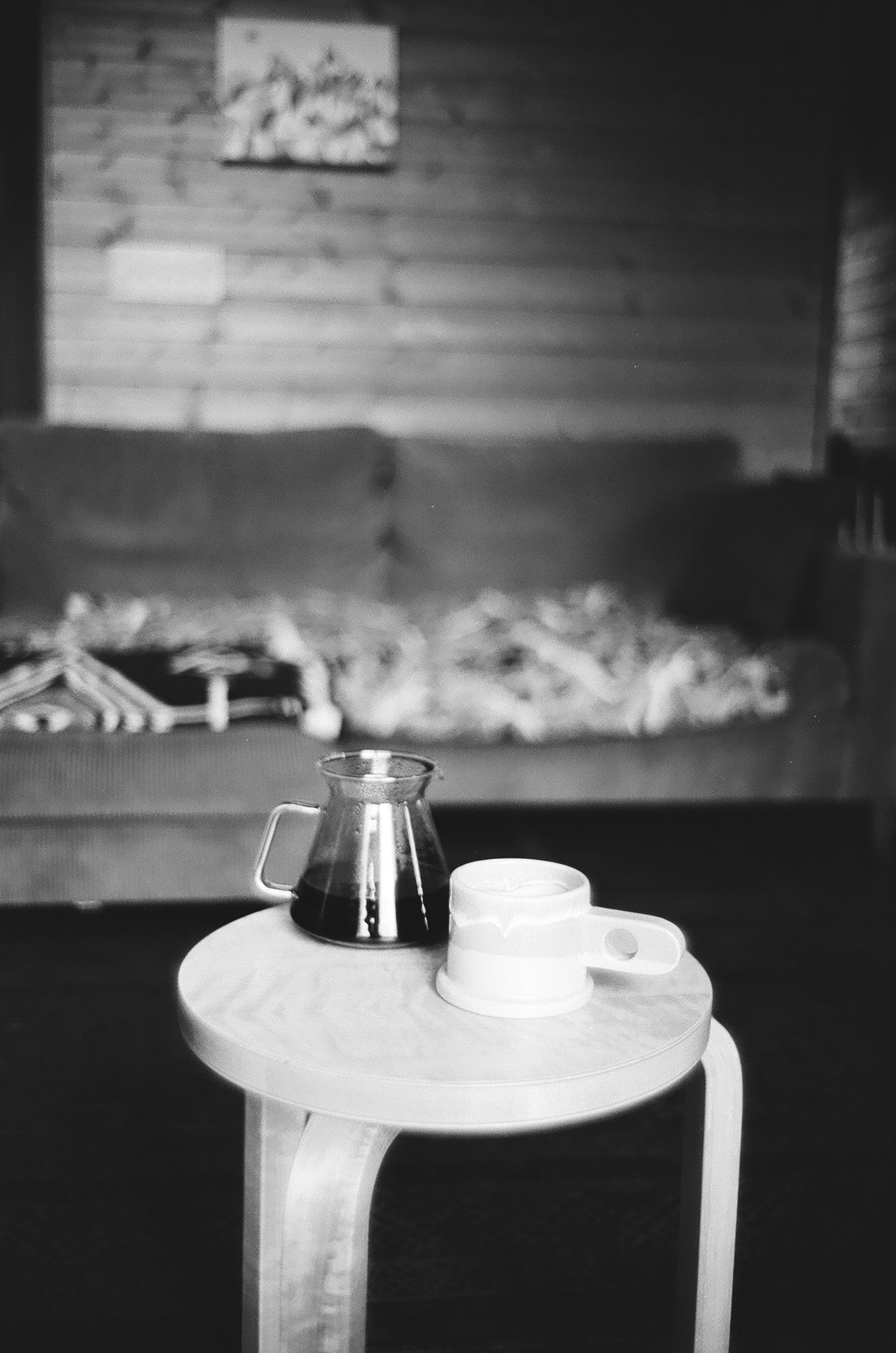 Una cafetera y una taza en una mesa pequeña con un sofá de madera al fondo