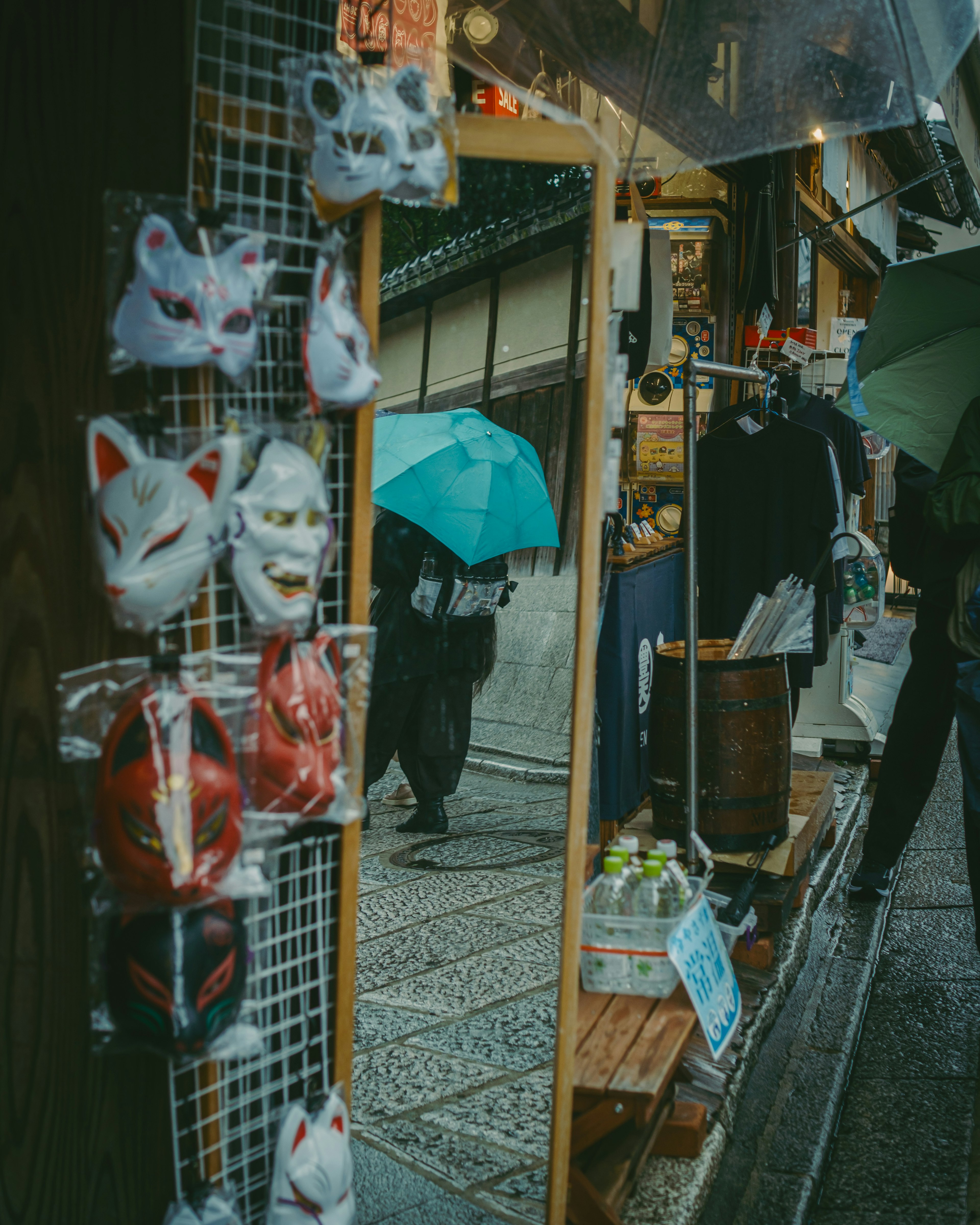 Traditional masks displayed in a rainy street market with a person holding an umbrella