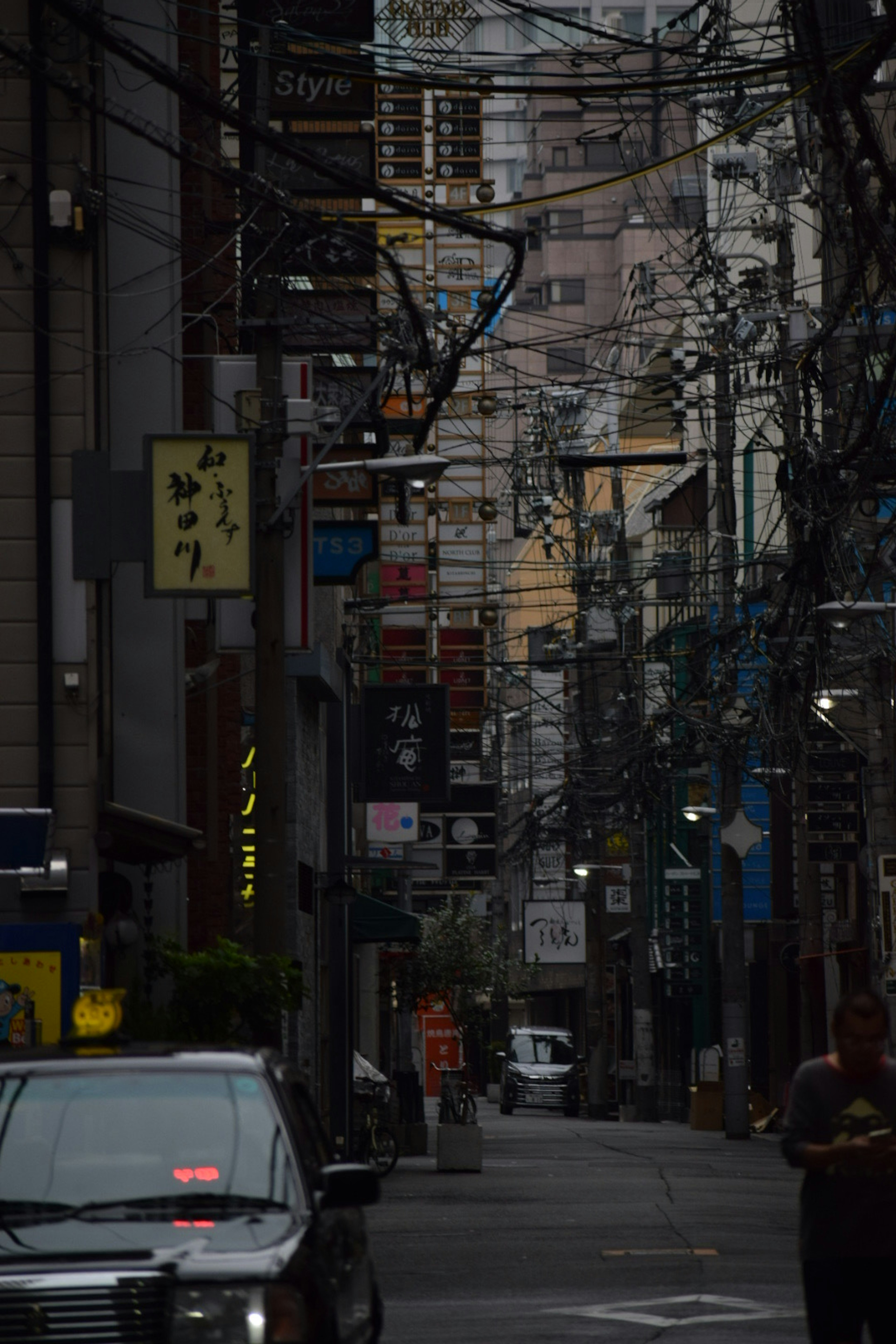 暗い路地に並ぶ看板と電線が特徴的な都市の風景