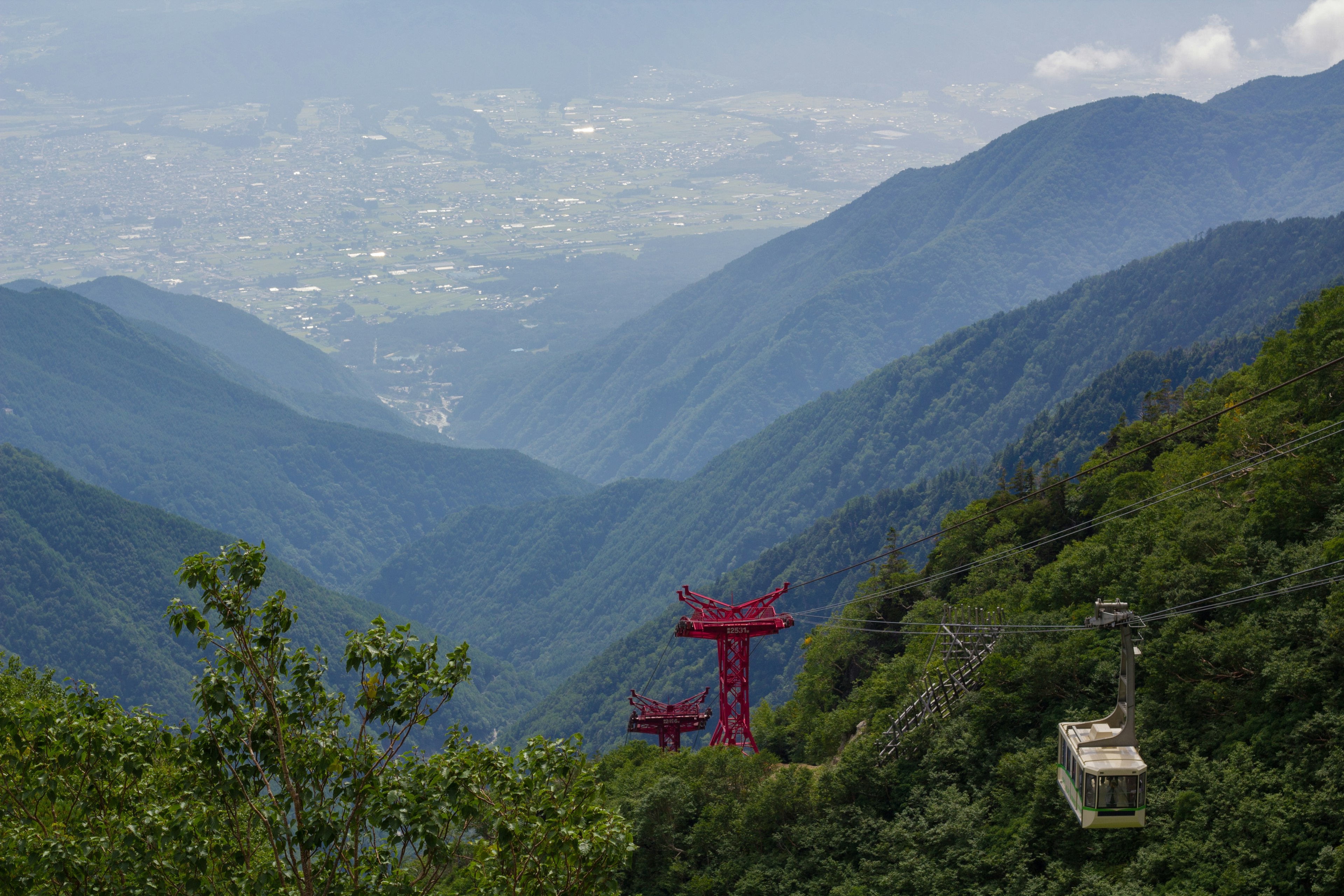 Vista escénica de montañas con un teleférico rojo y vegetación exuberante