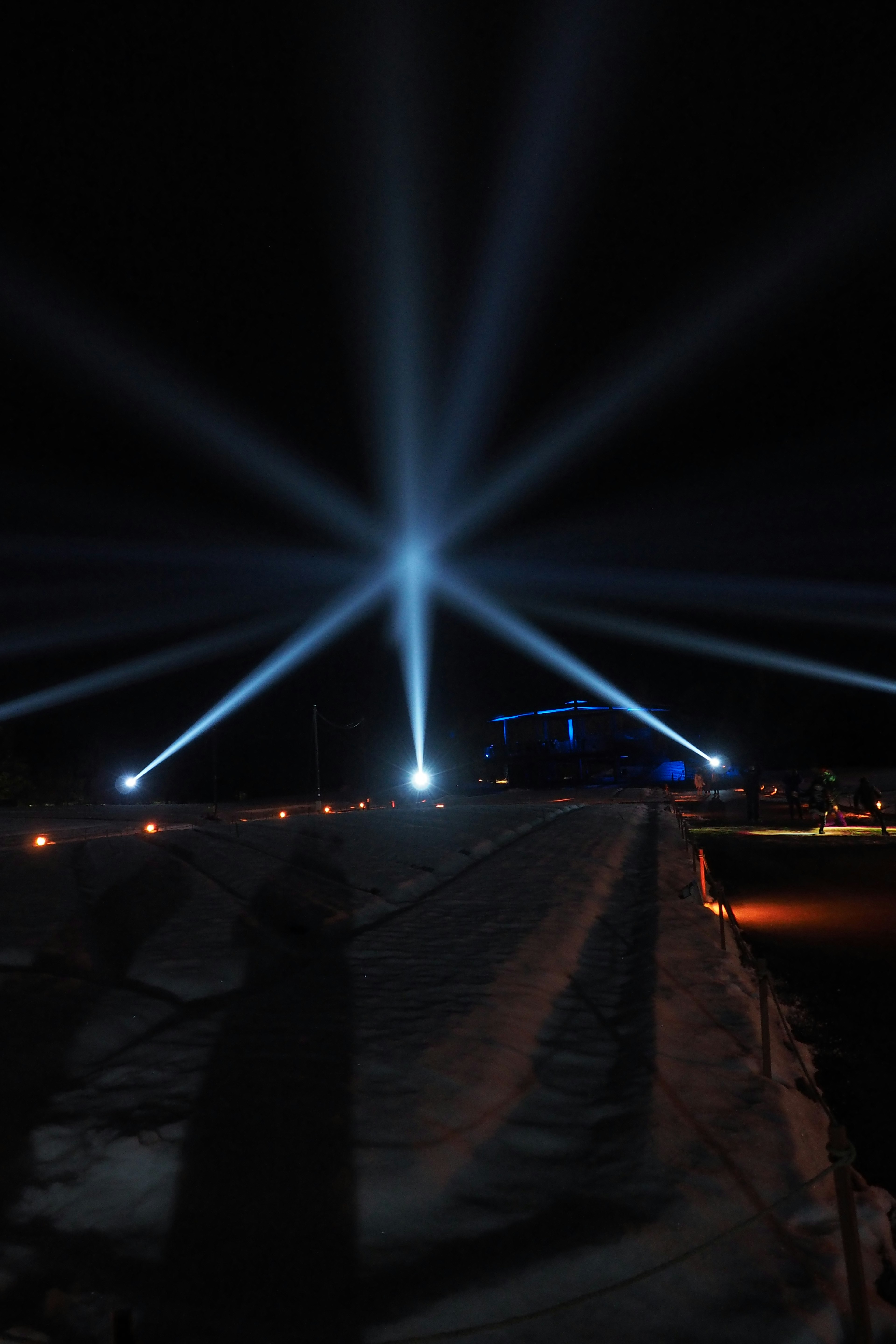 Blue beams of light radiating in the night sky with a shadowy path