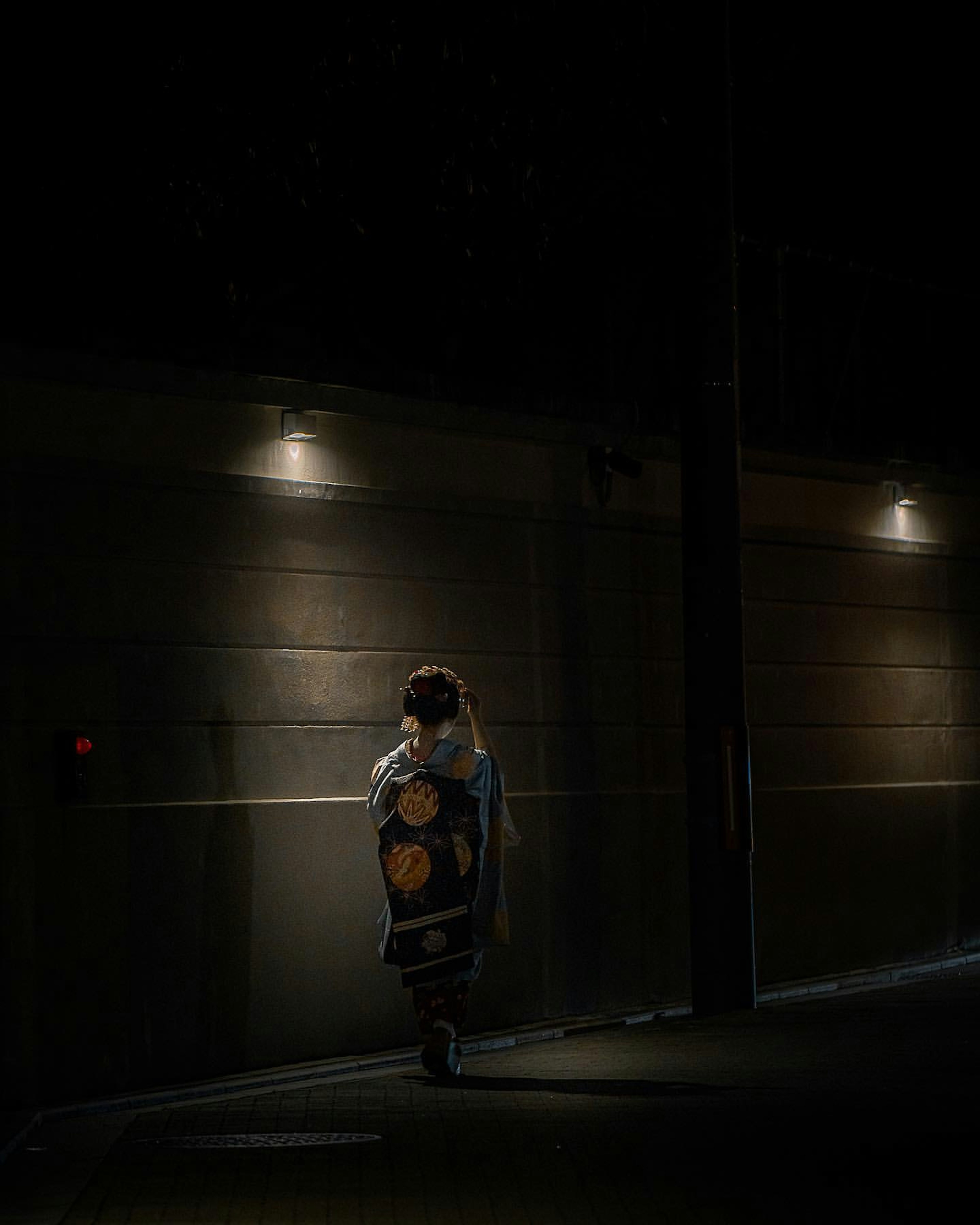 Silhouette of a person walking down a dark alley with lights in the background