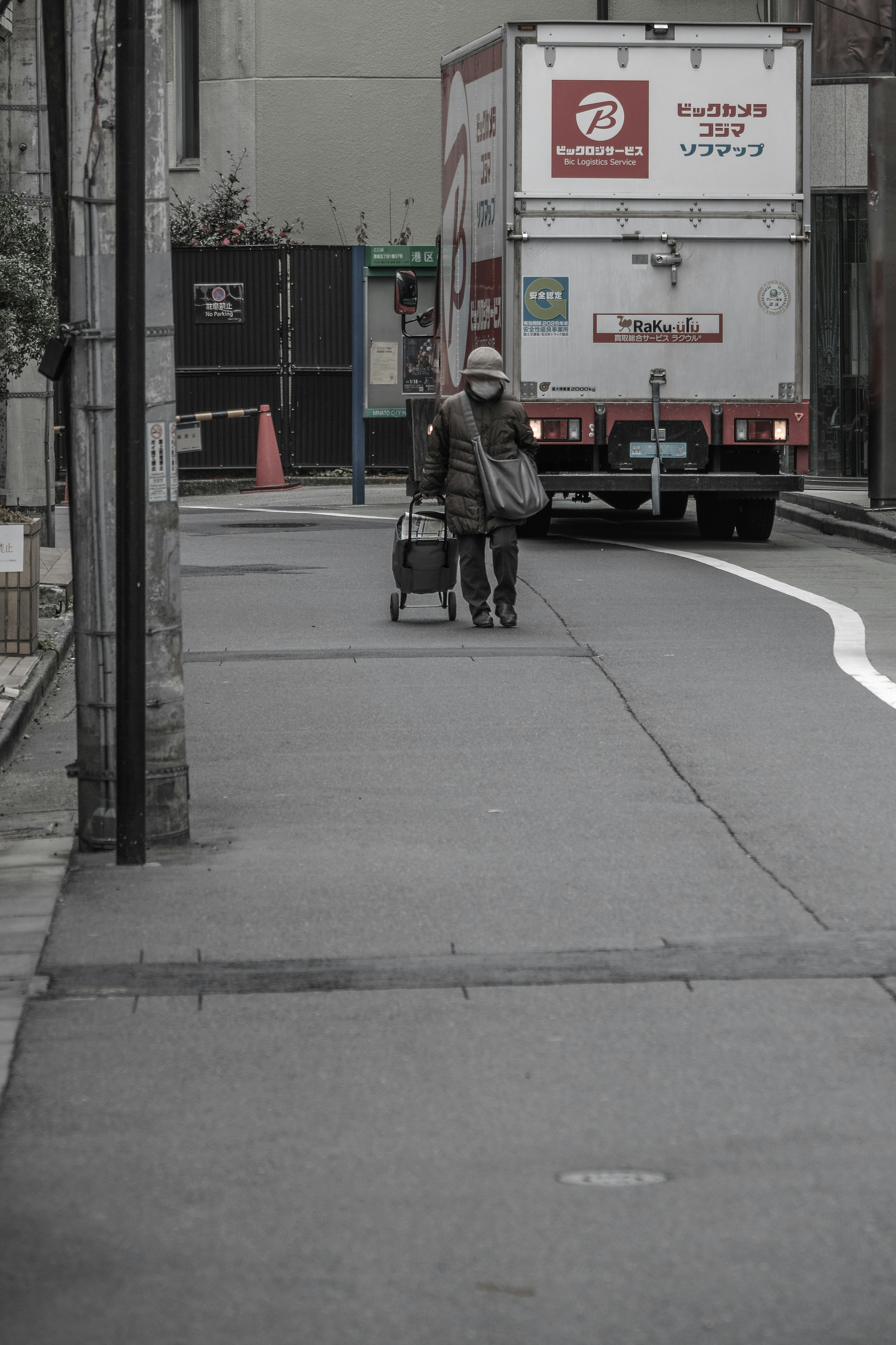 A person walking with luggage at a street corner with a truck in the background