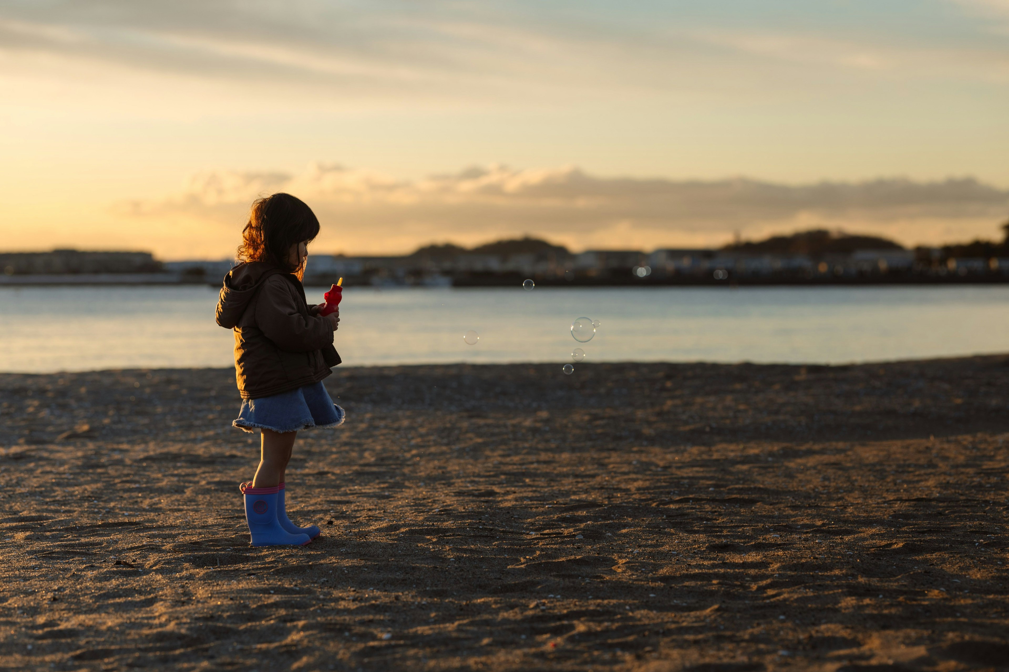 夕日を背景に砂浜に立つ子供が赤いおもちゃを持っている