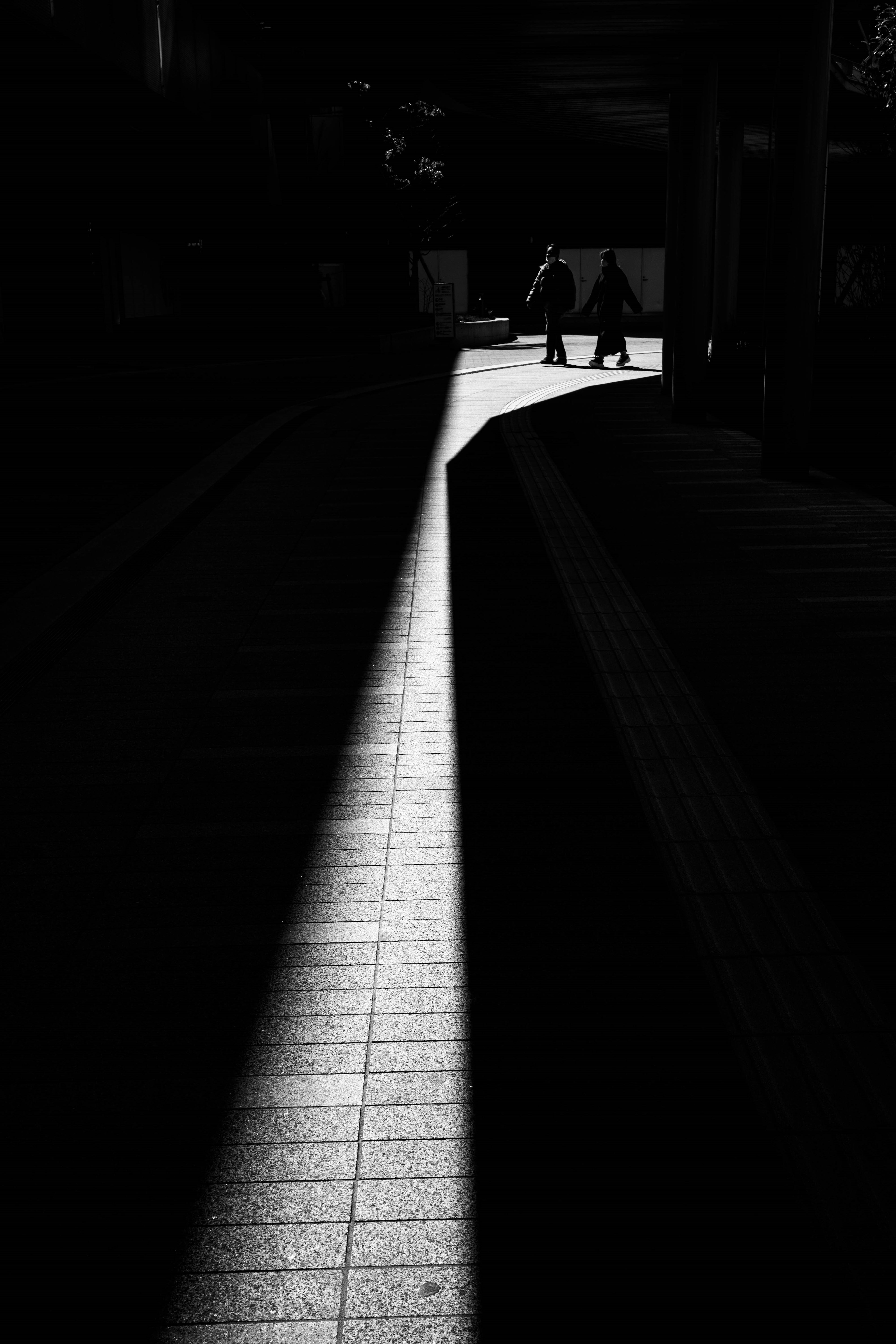 Urban scene with a bright light beam contrasting against a dark background featuring silhouettes of people