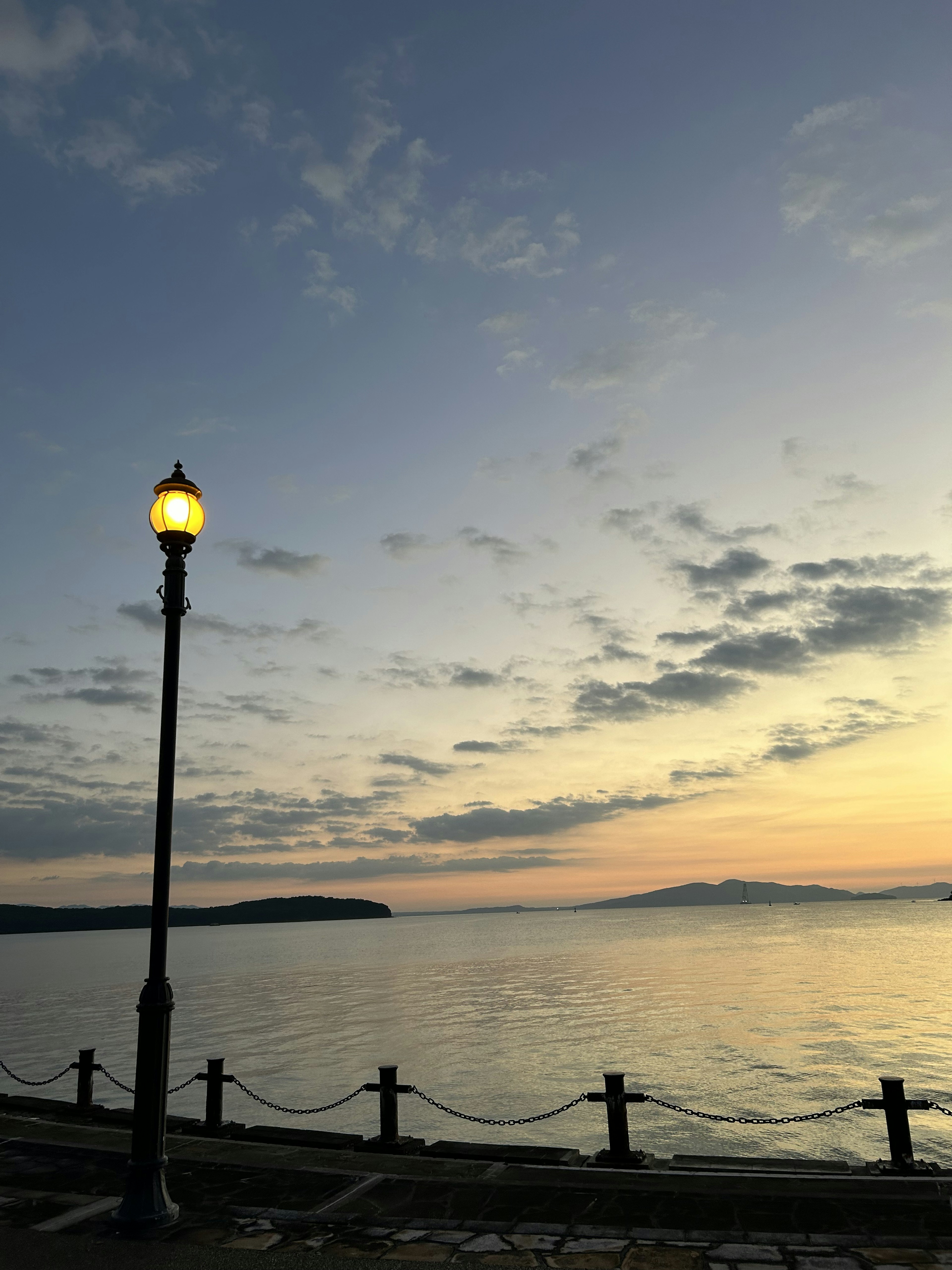 夕暮れ時の海岸沿いの街灯と穏やかな水面