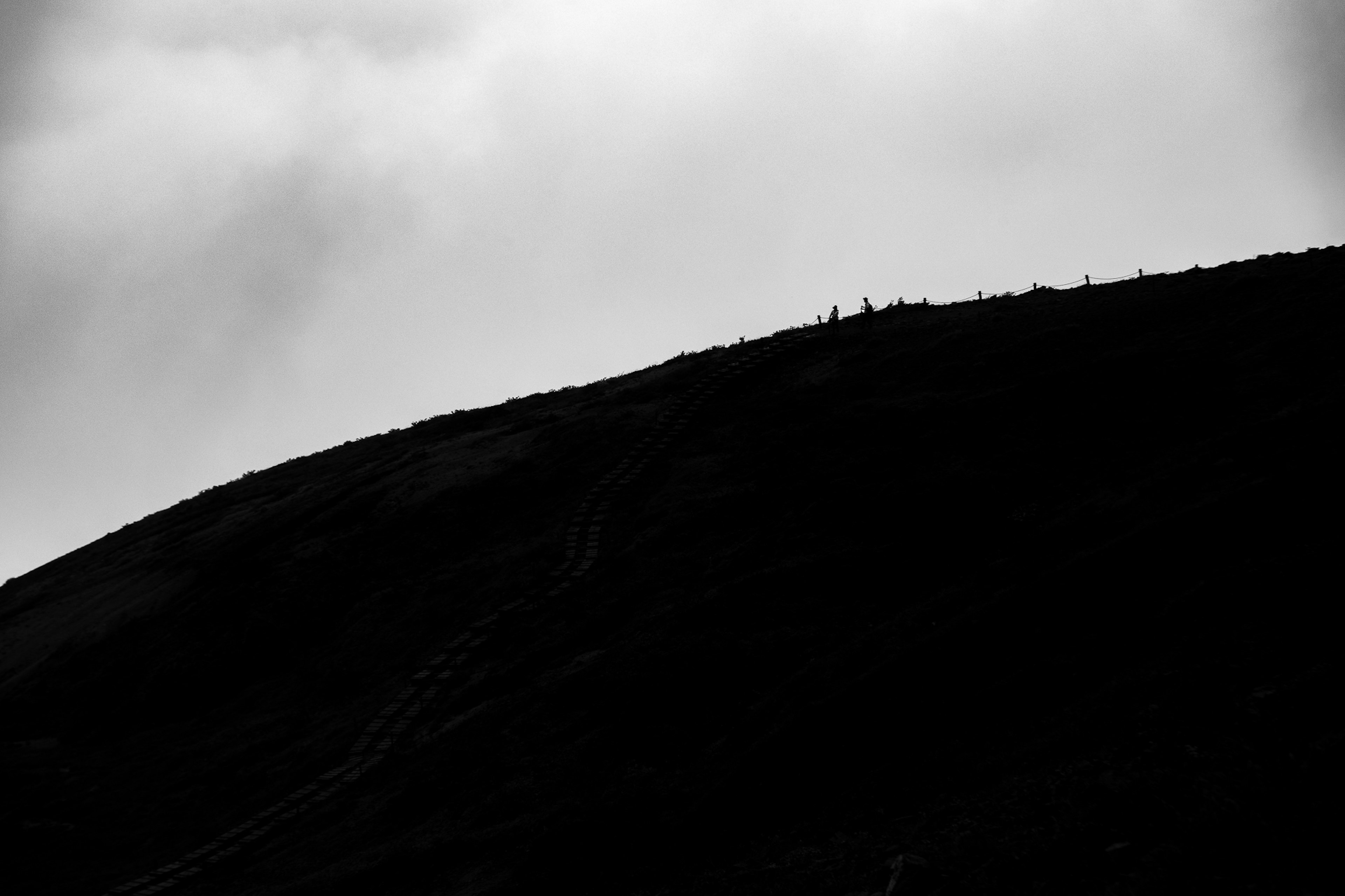 Siluet puncak gunung dengan sosok kecil di latar belakang langit mendung