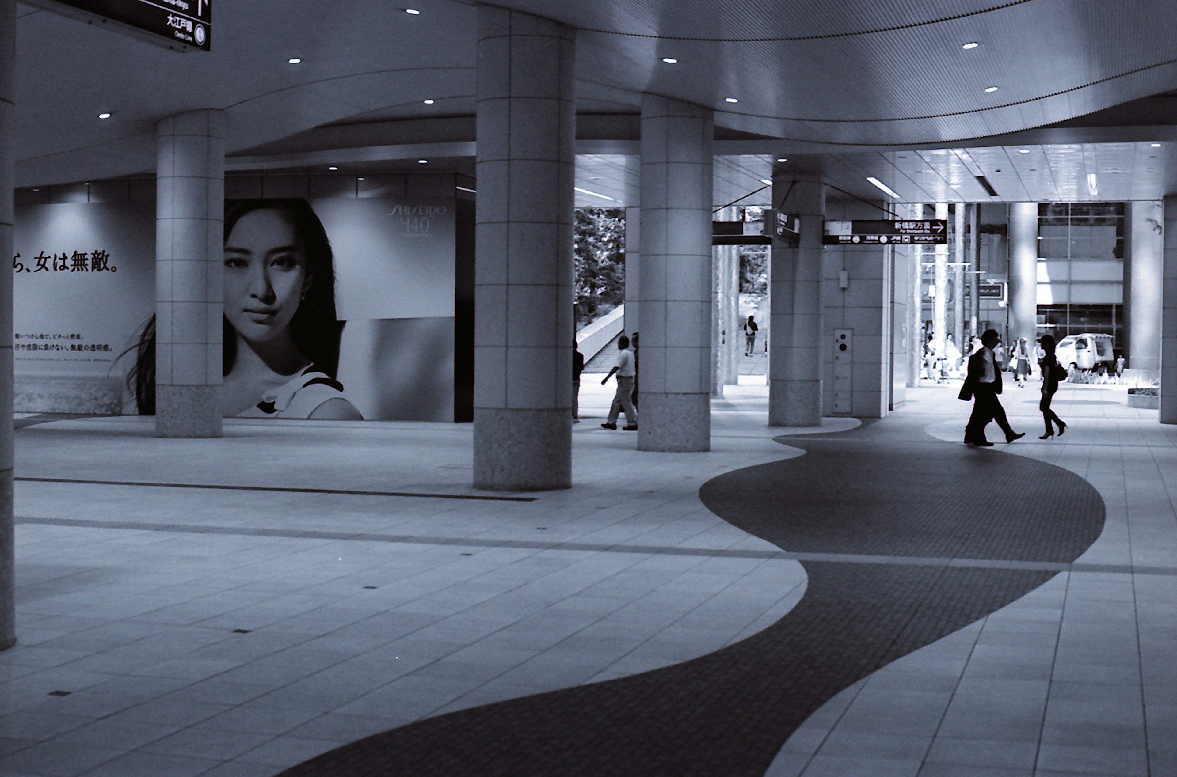 Espace urbain monochrome avec des personnes marchant et une grande affiche d'une femme