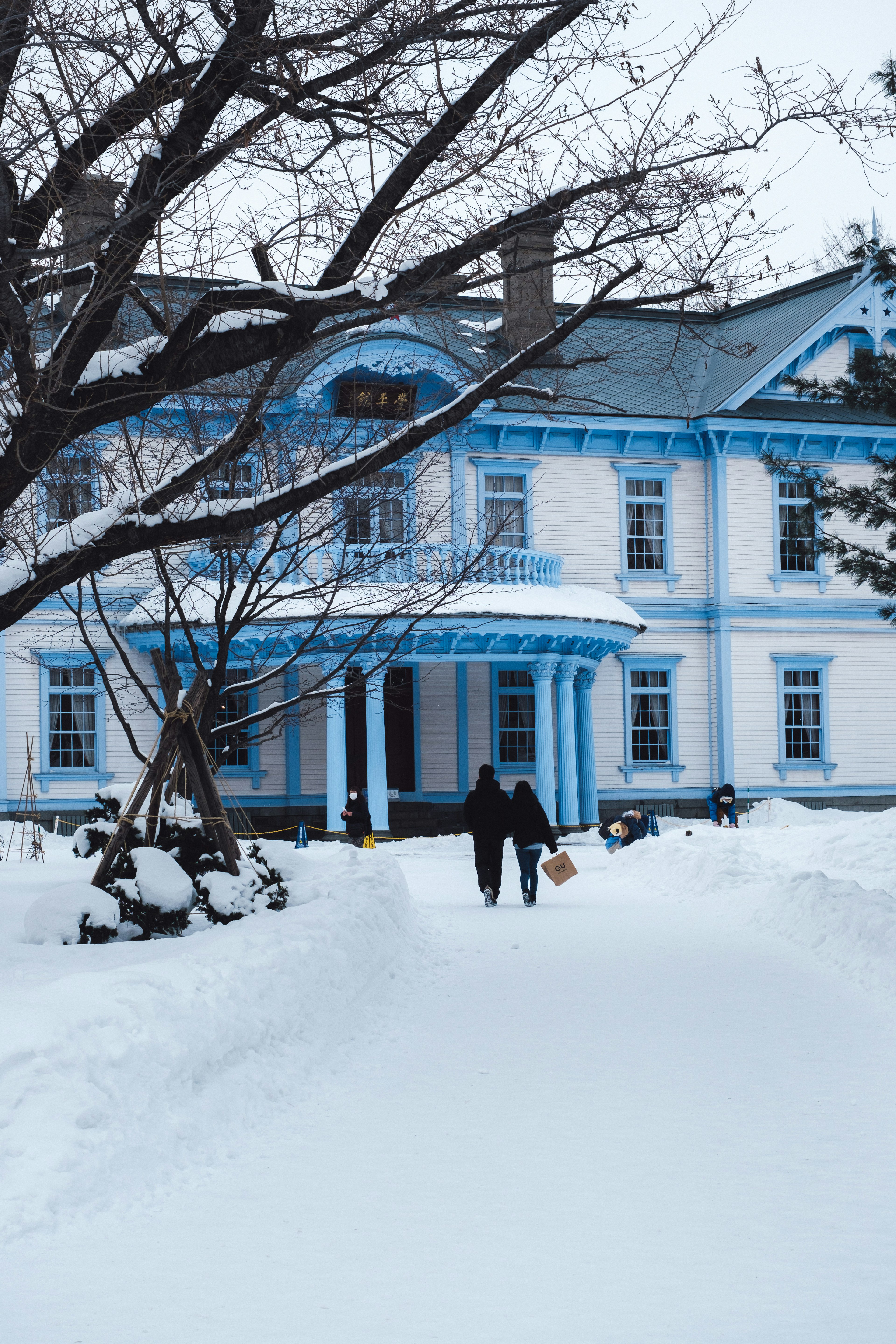 一對情侶在被雪覆蓋的藍白色建築前手牽手