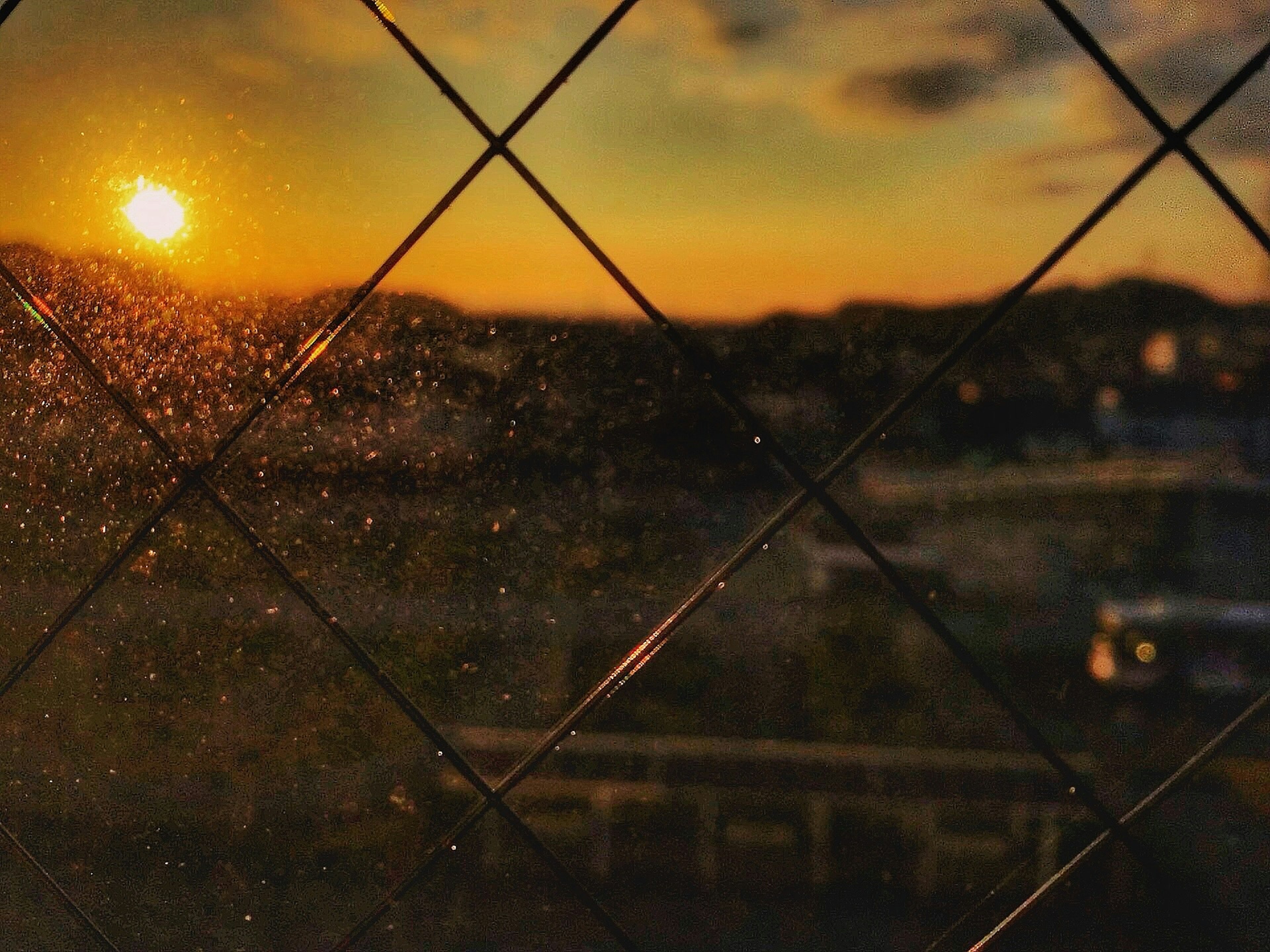 Sunset view through a window with diamond-shaped glass panes and a blurred landscape