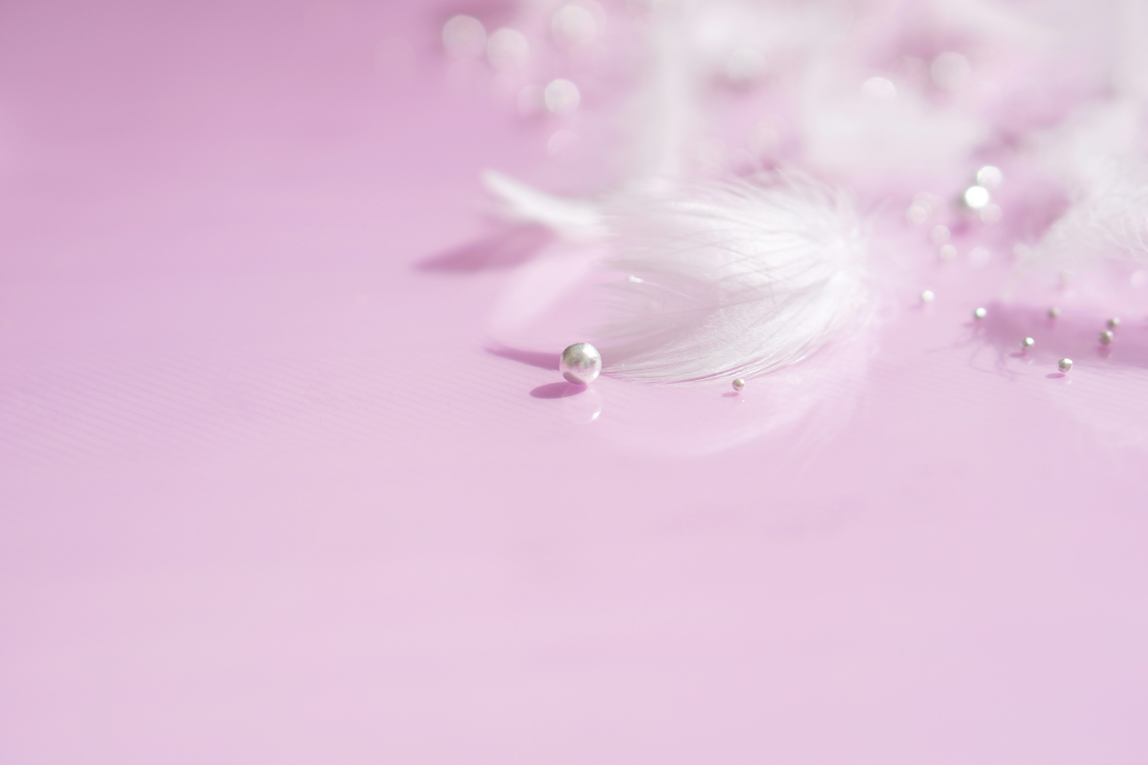 Soft pink background with scattered white feathers and pearls