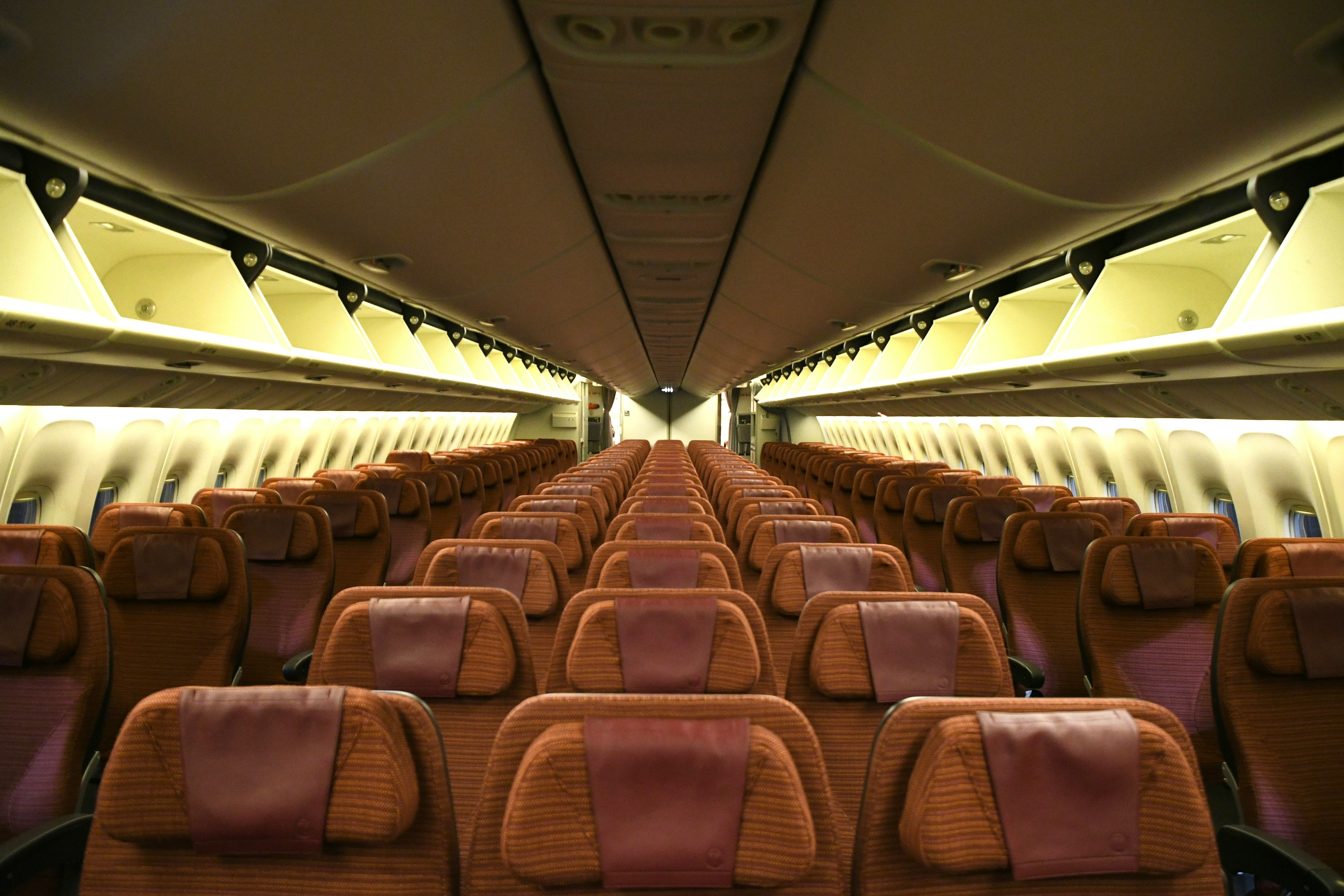 Intérieur d'un avion avec des rangées de sièges marron et un éclairage lumineux