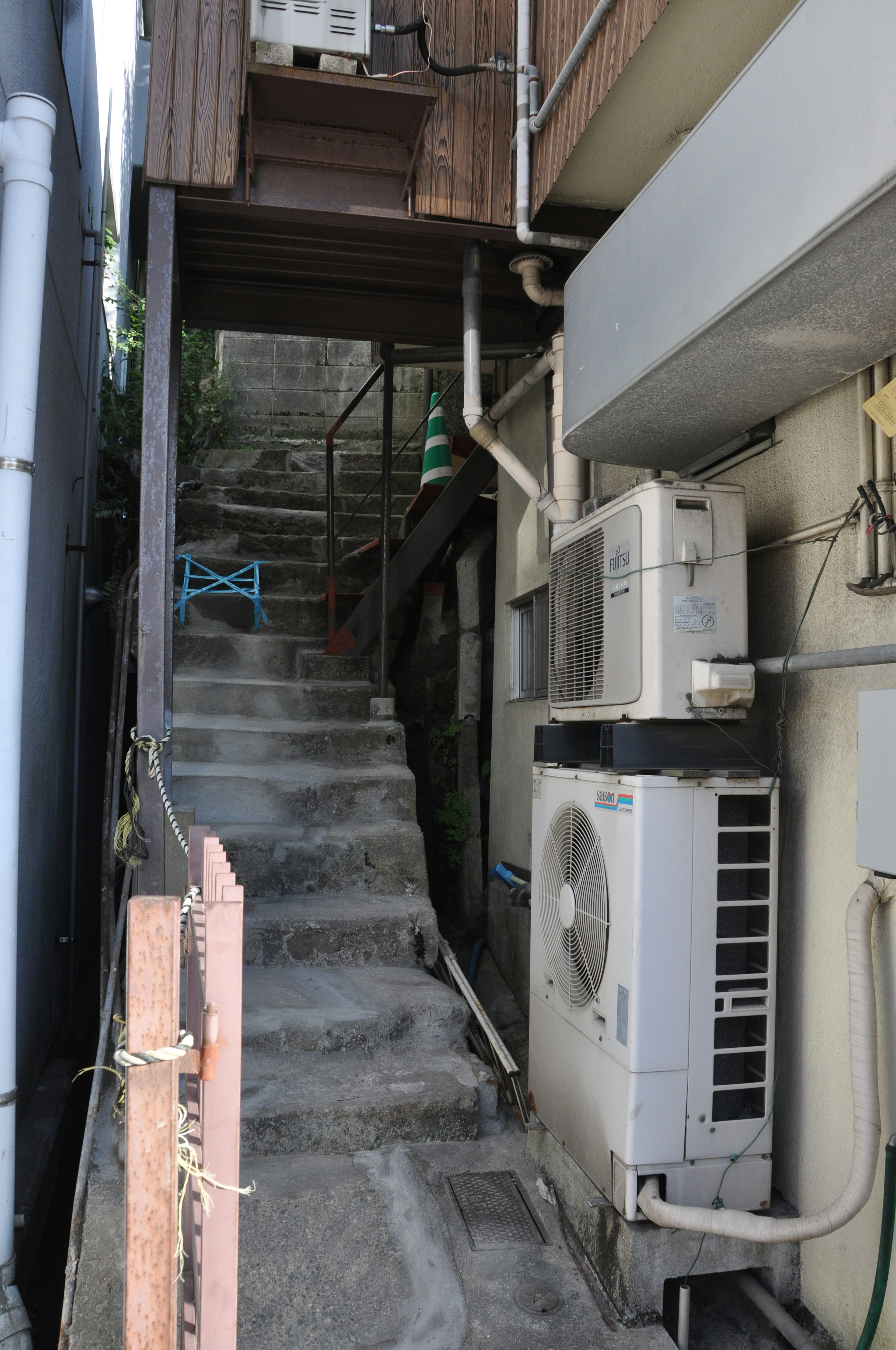 Chemin étroit avec des escaliers et une unité de climatisation à côté d'un bâtiment commercial