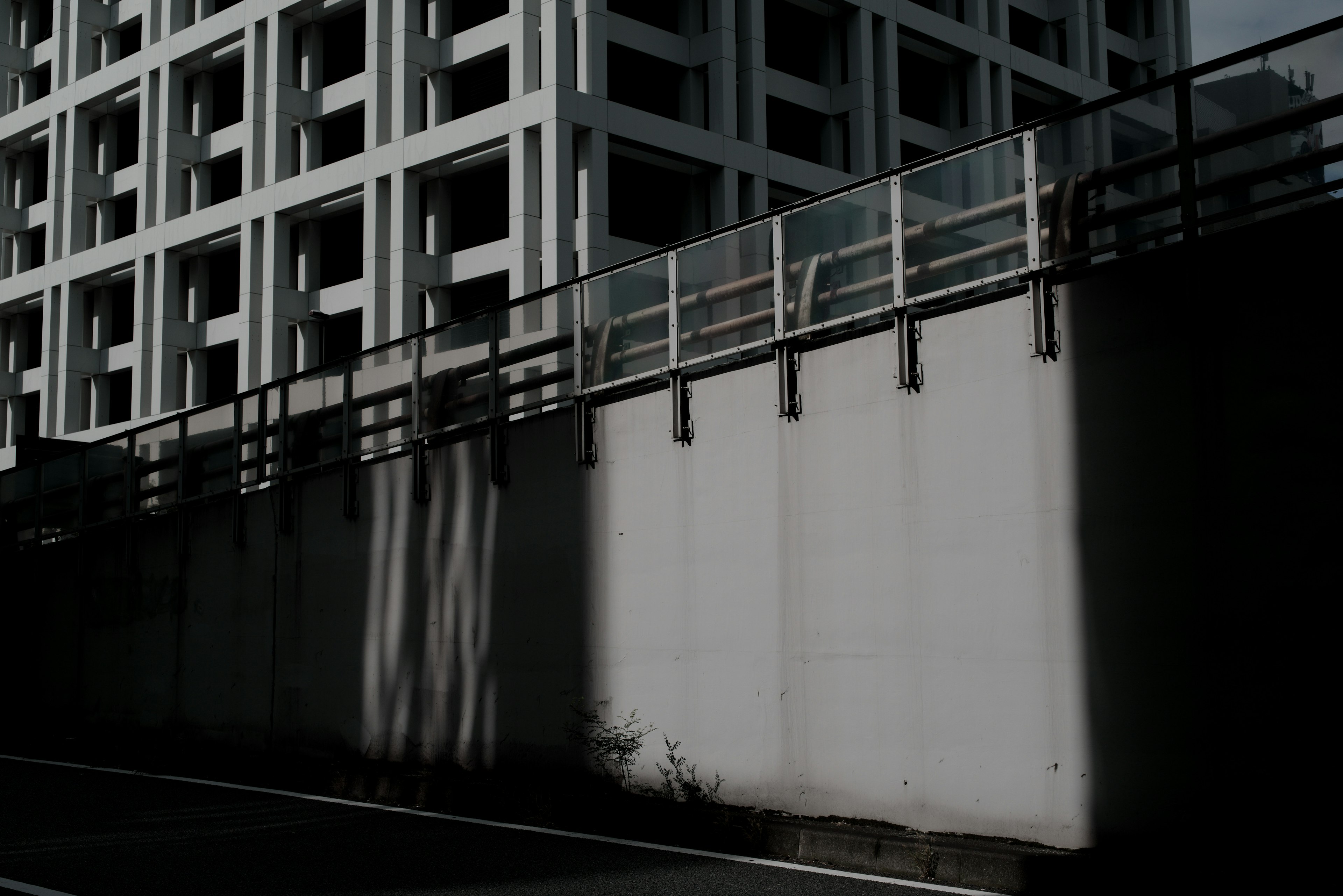 Photo of a concrete wall and fence with shadows of a high-rise building