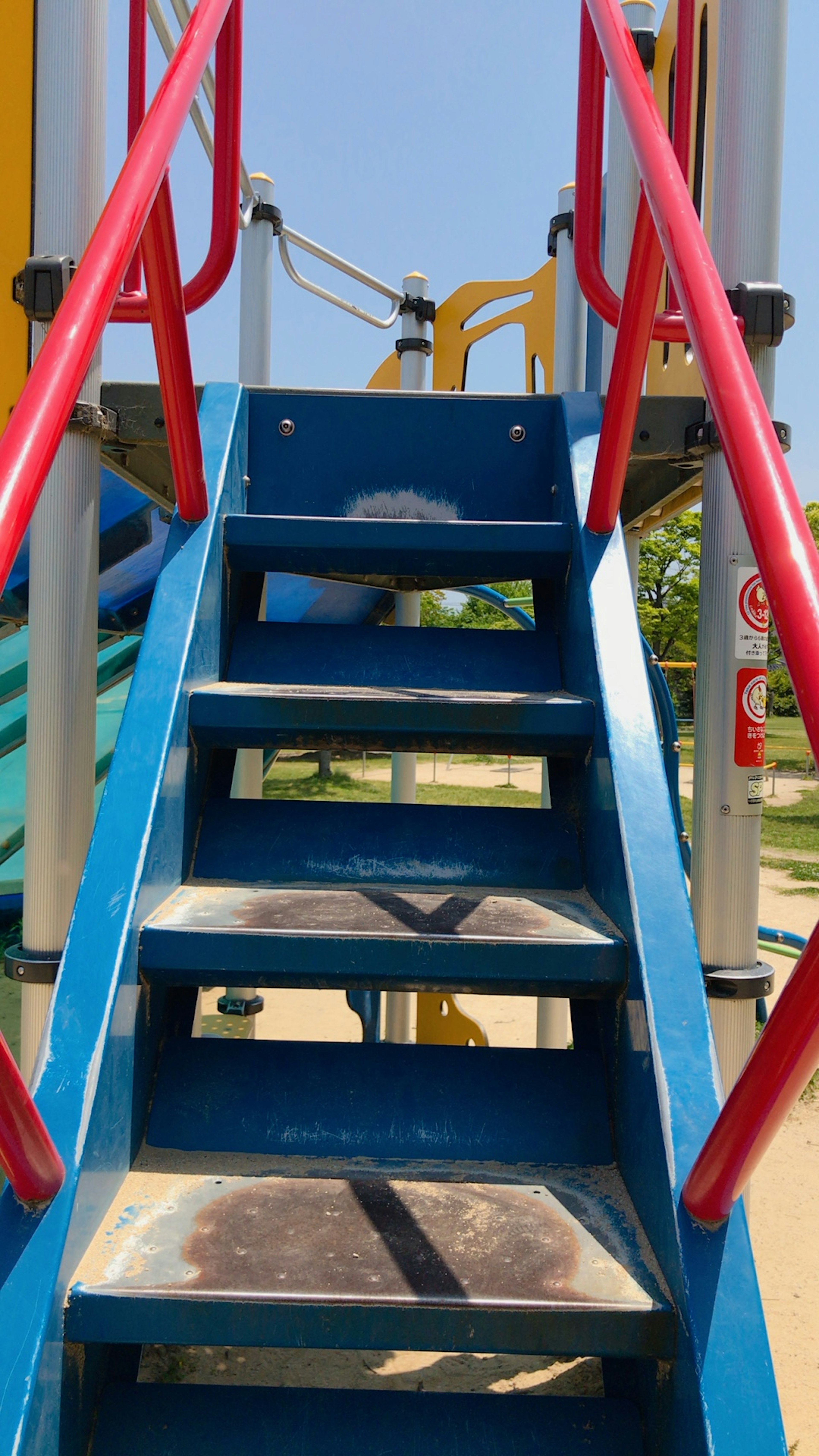 Escalier menant à un toboggan bleu avec des rampes rouges