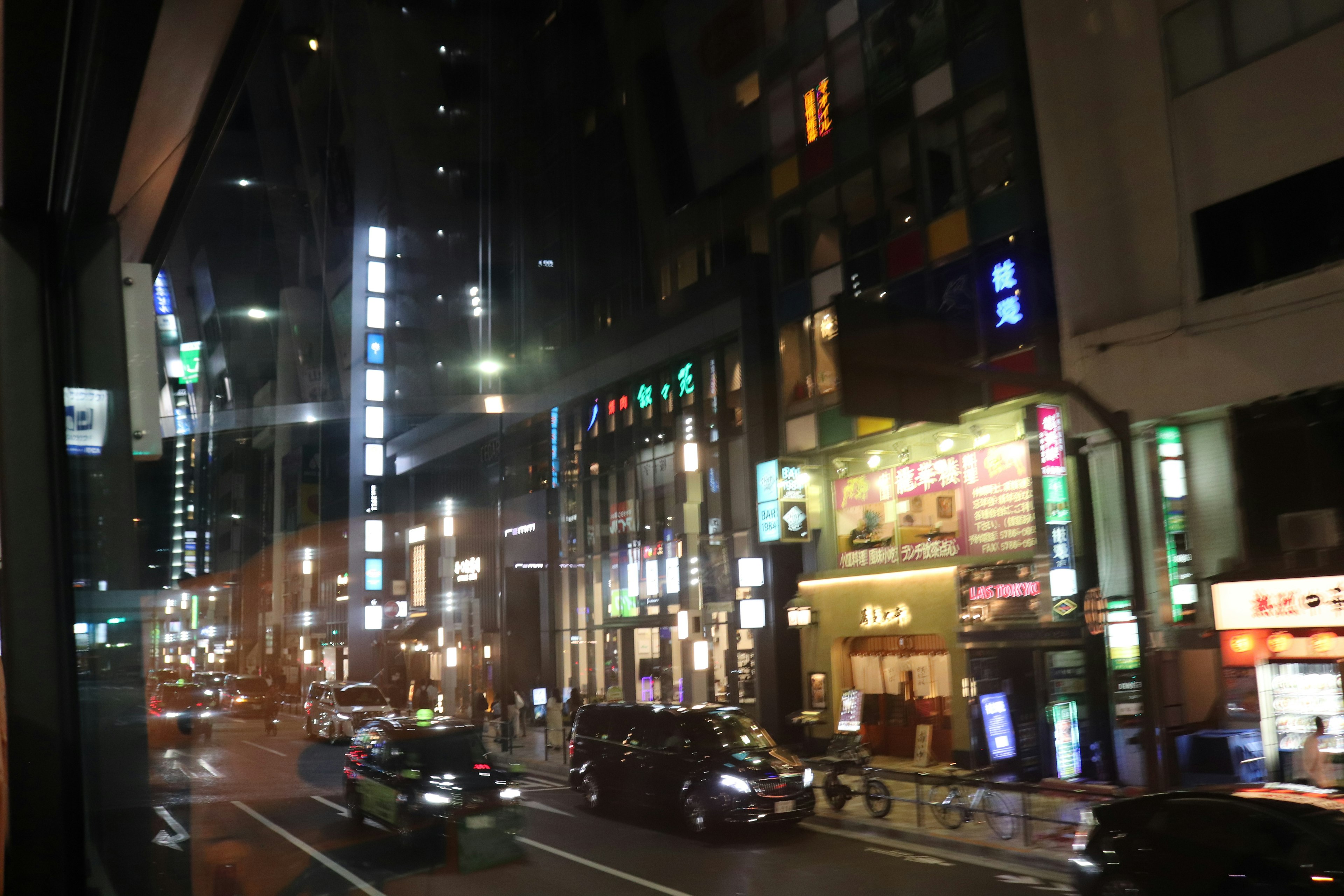 View of a city street at night seen through a window with glowing car lights and neon signs