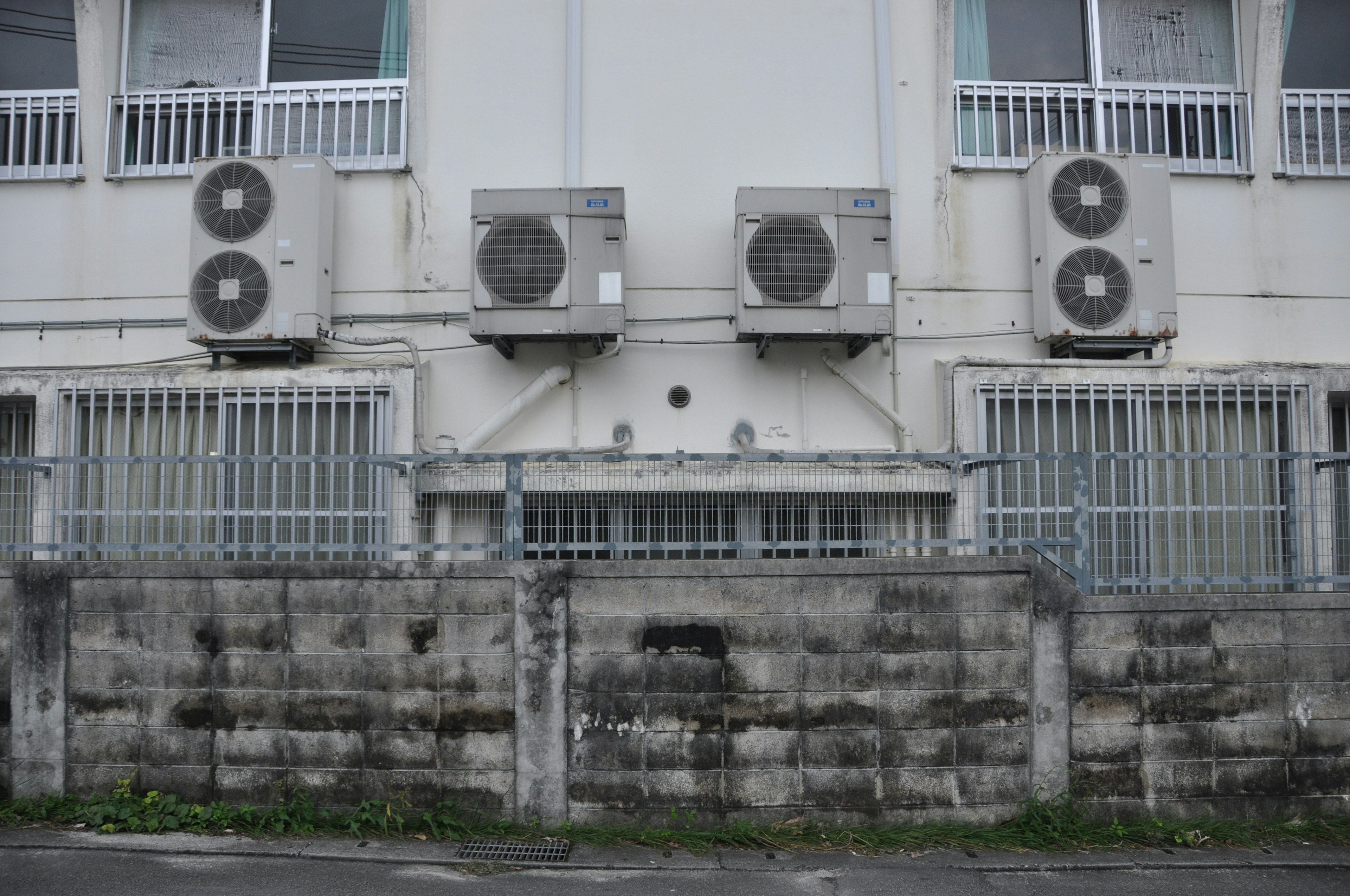 Air conditioning units mounted on a building's exterior wall with a metal fence