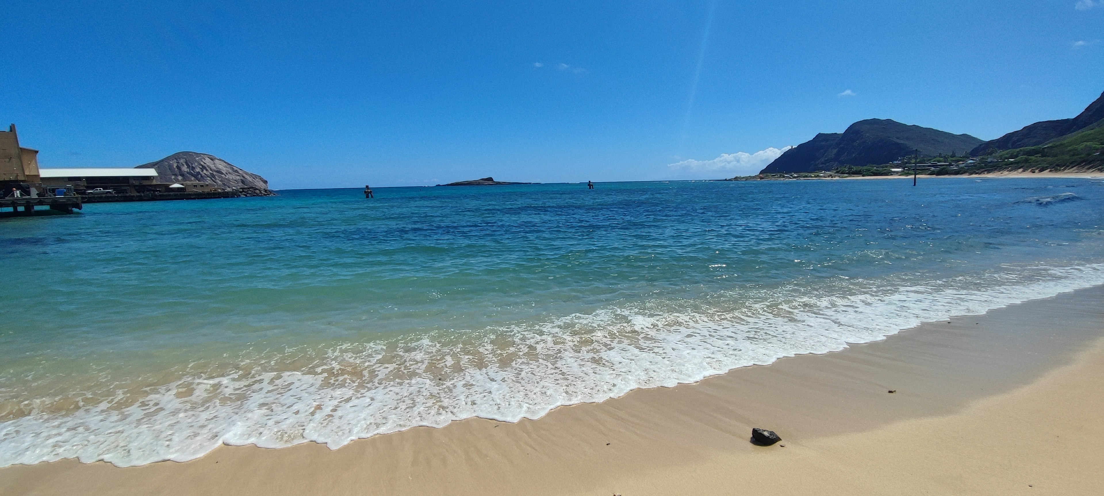 Malersiche Sicht auf den blauen Ozean und den weißen Sandstrand mit nahegelegenen Bergen und einem Pier