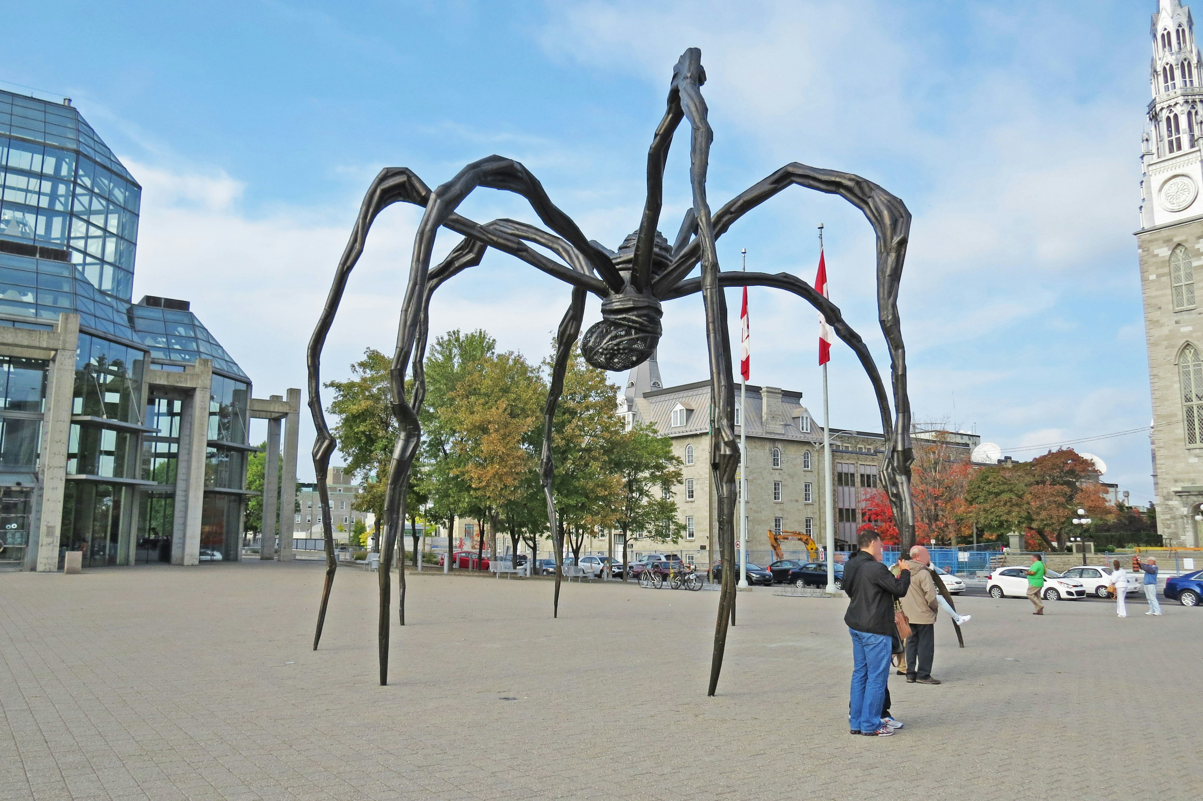 Une grande sculpture d'araignée se dresse dans une place avec des personnes à proximité