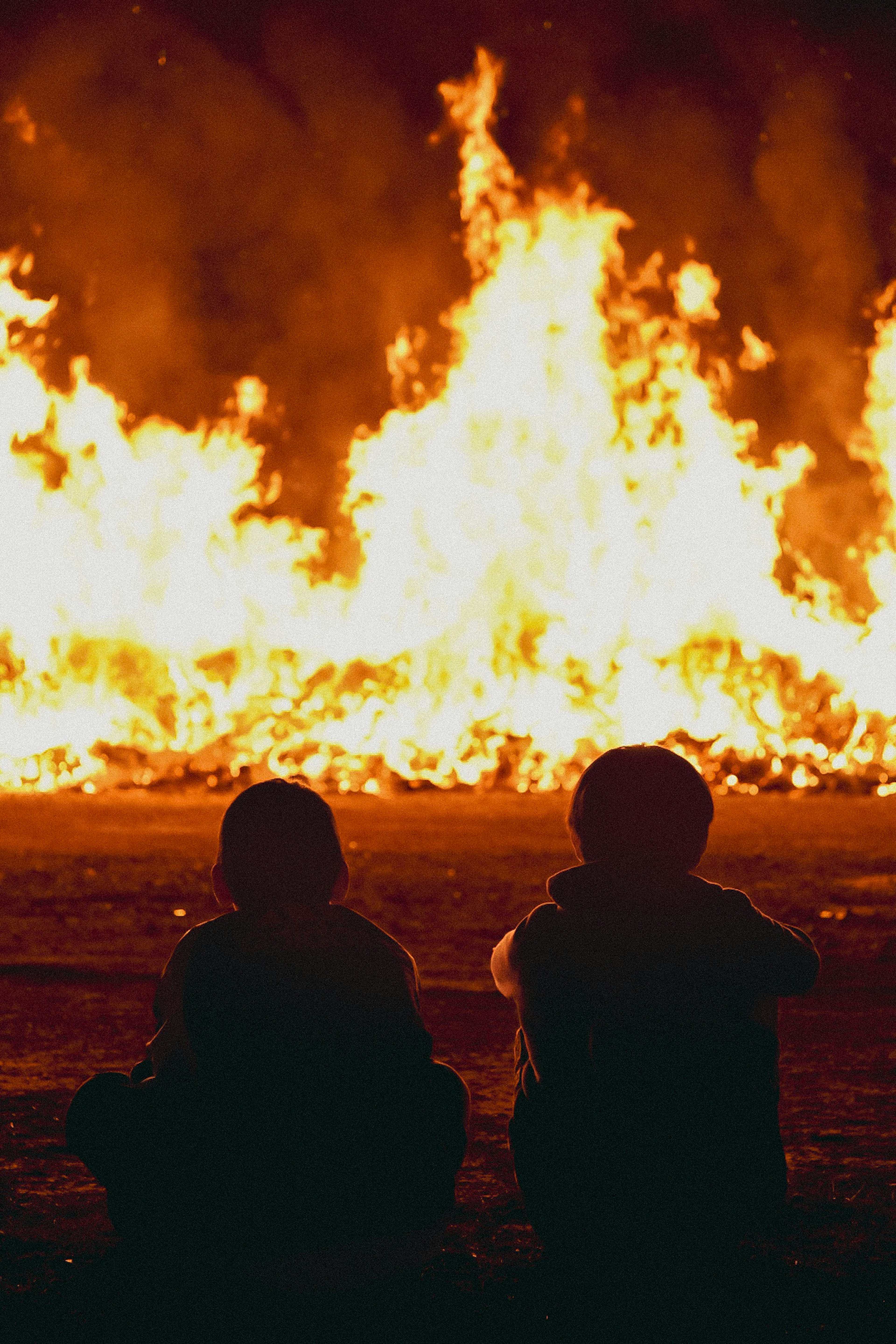 Two children sitting in front of a large fire