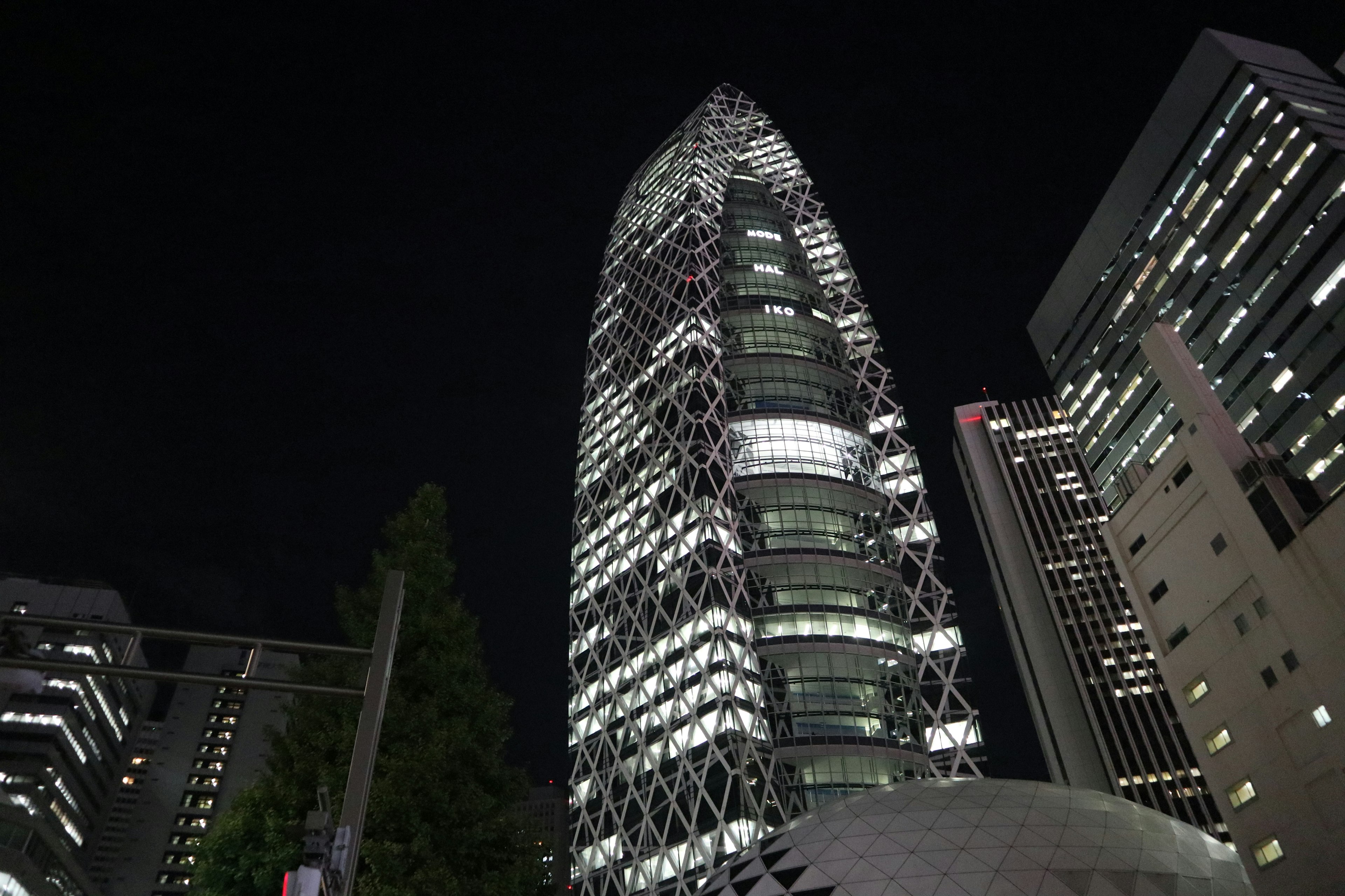 Sebuah gedung pencakar langit yang dirancang unik di Shinjuku pada malam hari dikelilingi oleh lampu kota